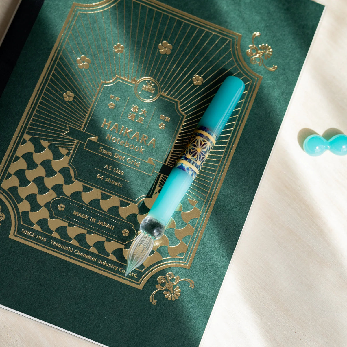 Turquoise Hemp Leaves glass dip pen on a green HAIKARA notebook cover with gold foil printing