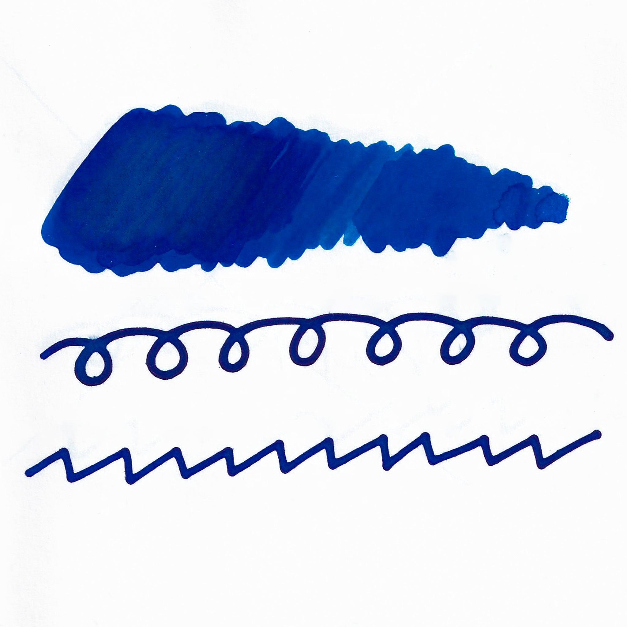 Swatch of blue fountain pen ink on white paper. The ink shows shading variations, with a dark center and lighter edges. Below are wavy and looped lines demonstrating the ink's flow.  