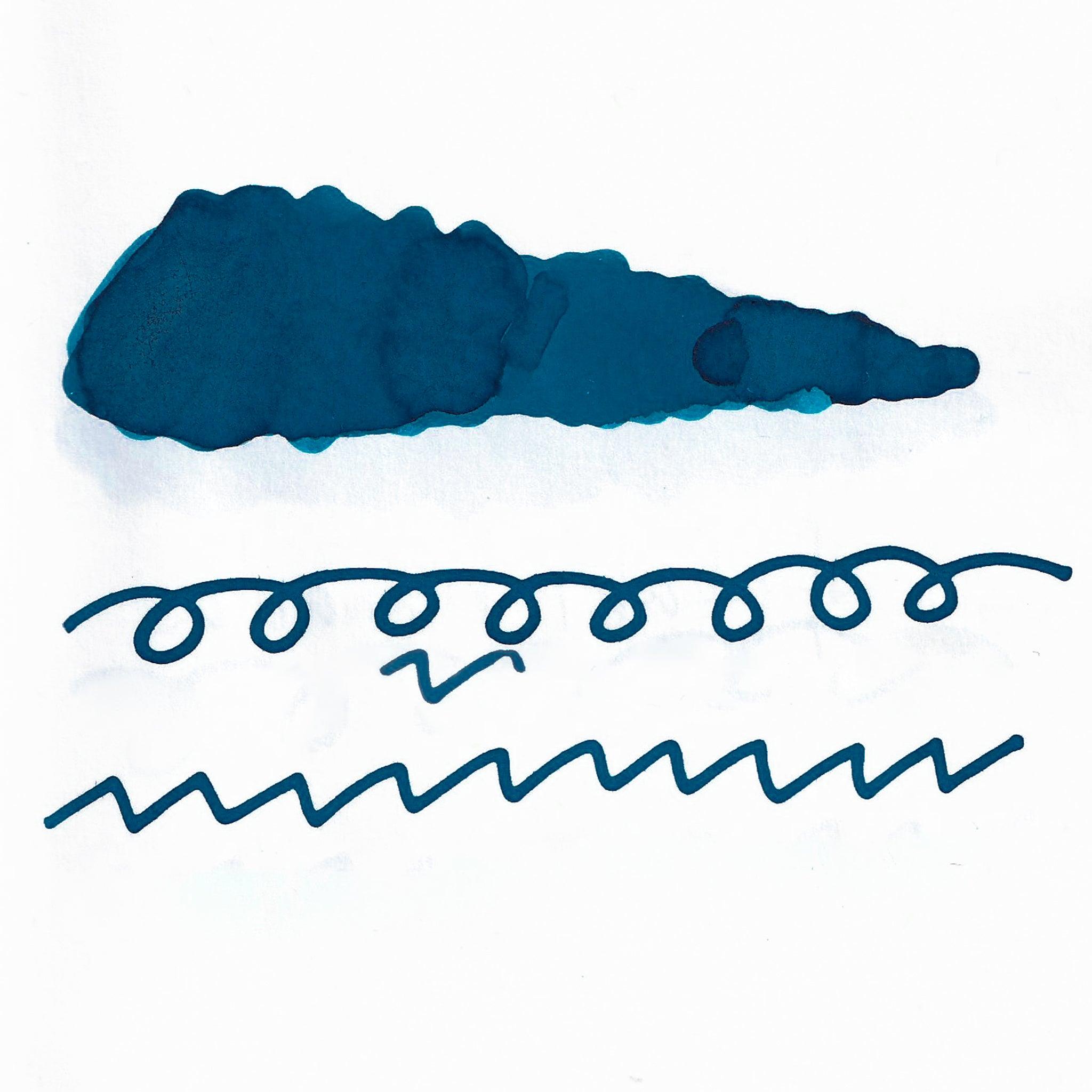 Swatch of deep blue fountain pen ink on white paper. The ink shows shading variations, with a dark center and lighter edges. Below are wavy and looped lines demonstrating the ink's flow.  