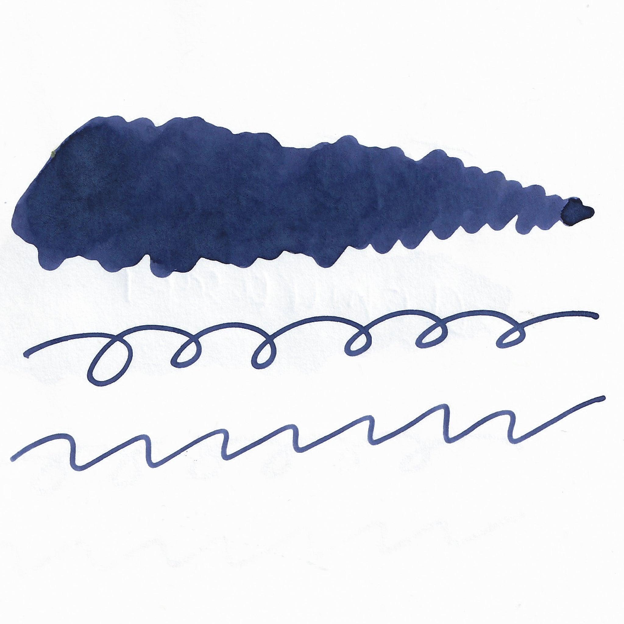 Swatch of blue fountain pen ink on white paper. The ink shows shading variations, with a dark center and lighter edges. Below are wavy and looped lines demonstrating the ink's flow.  