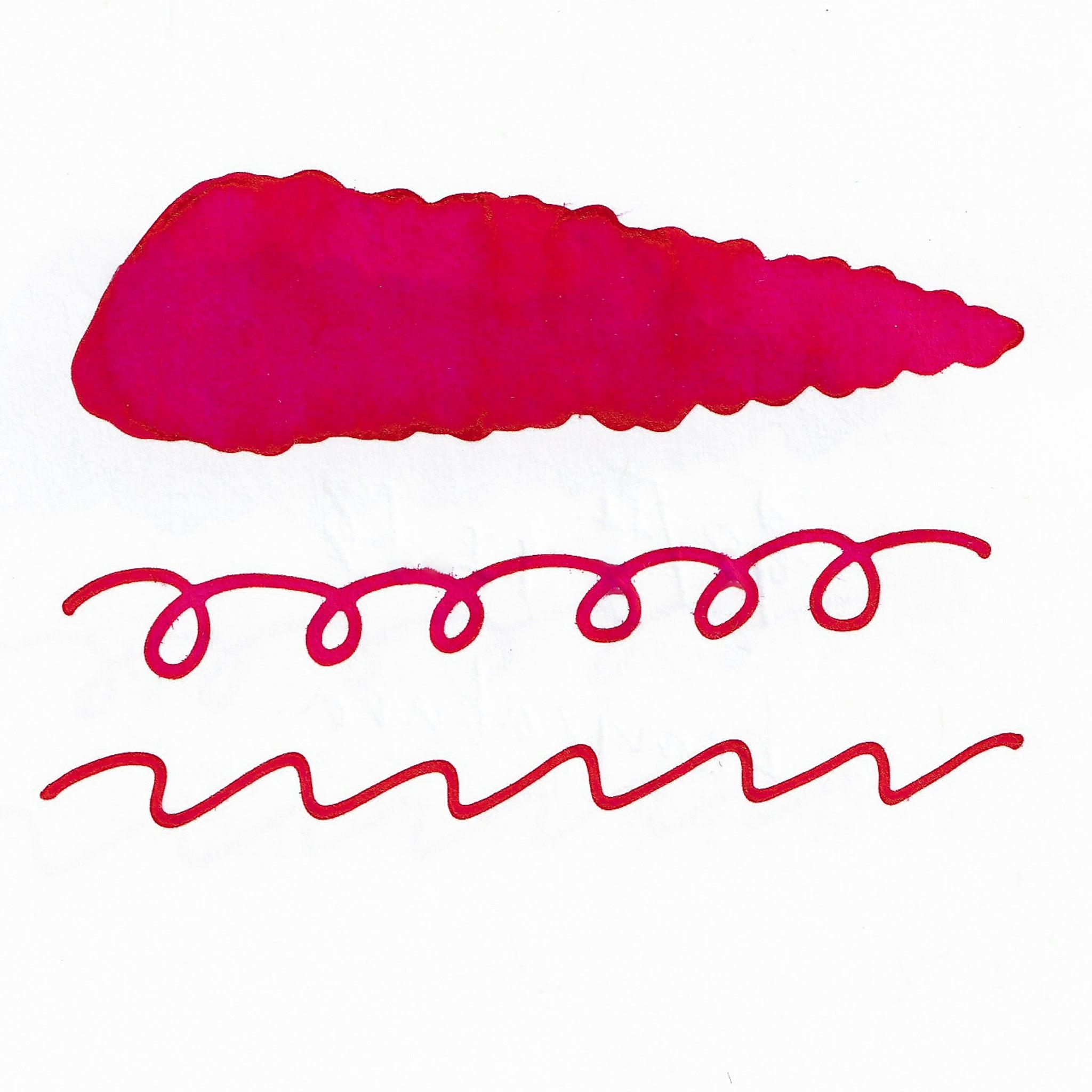 Swatch of red fountain pen ink on white paper. The ink shows shading variations, with a dark center and lighter edges. Below are wavy and looped lines demonstrating the ink's flow.  