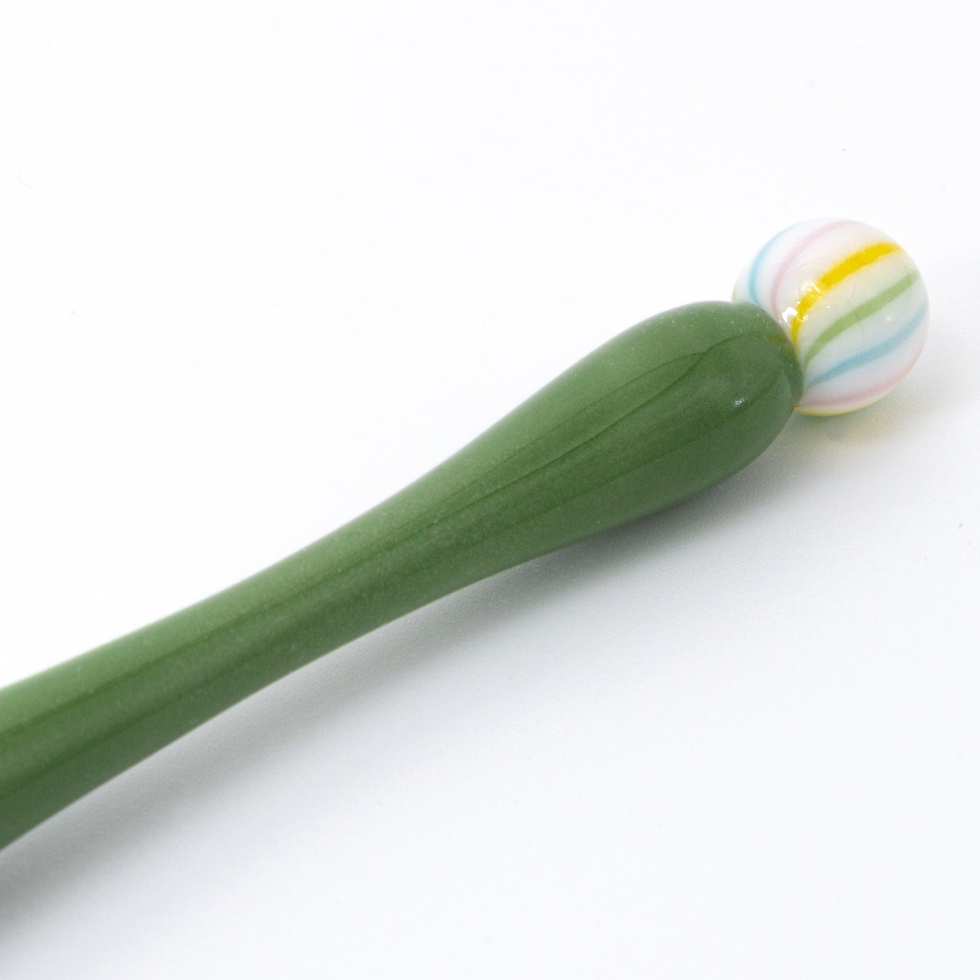 A close-up of a green matcha color glass pen with a colorful marble-like detail on both ends, resting on a clean, white background.