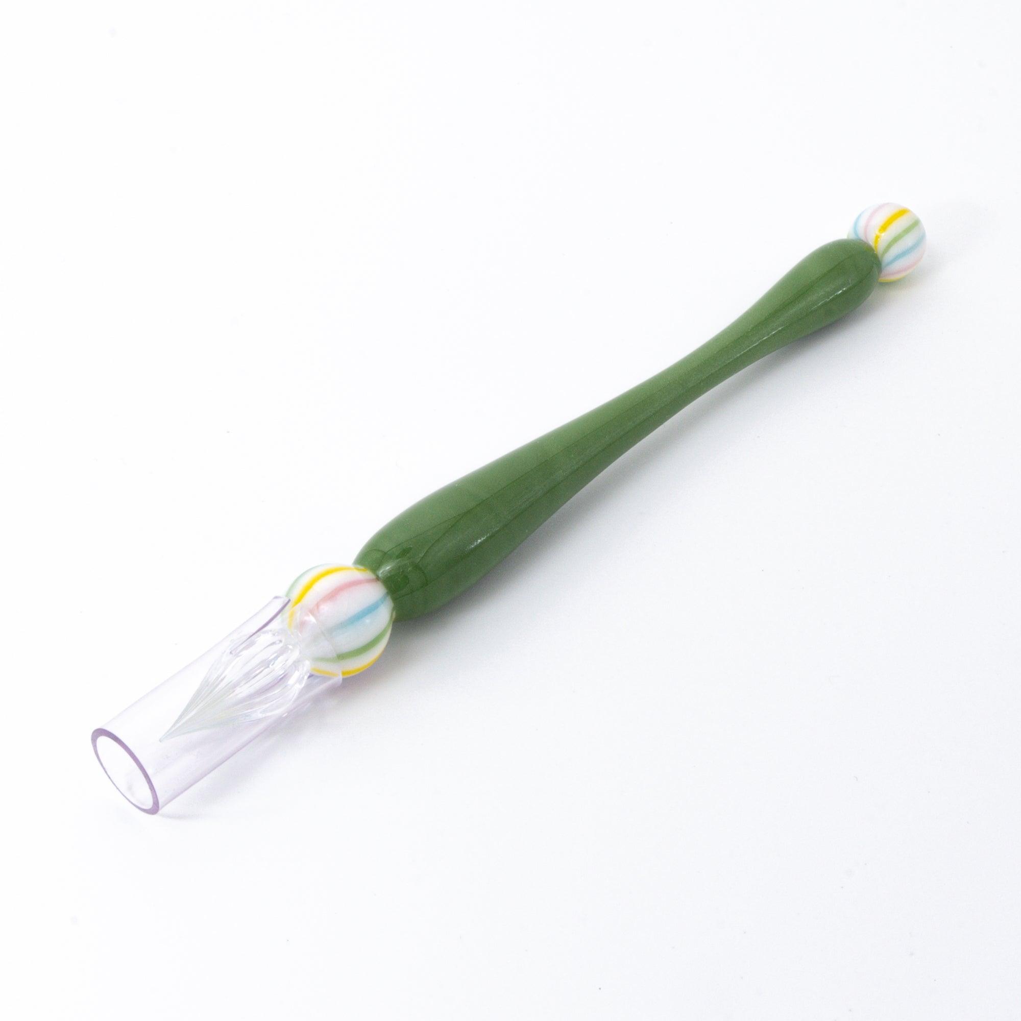 A close-up of a green matcha color glass pen with a colorful marble-like detail on both ends, resting on a clean, white background.