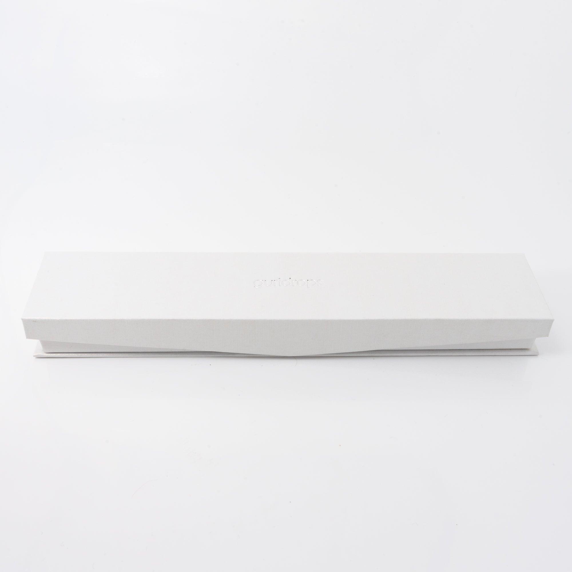 A white Guridrops branded box designed for a glass pen, photographed on a white surface with subtle reflections, providing a sleek and minimalist presentation.