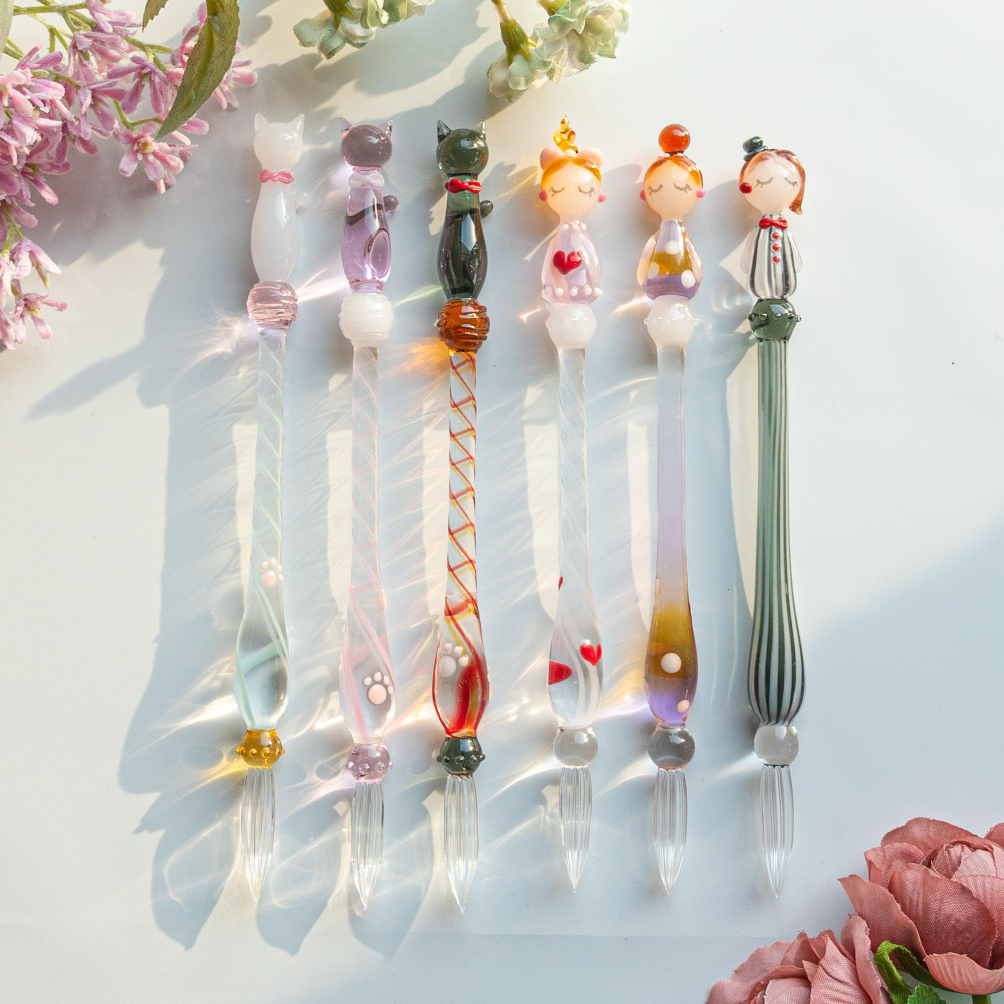 A whimsical set of glass dip pens featuring cats and human figures, capturing the charm of their playful designs