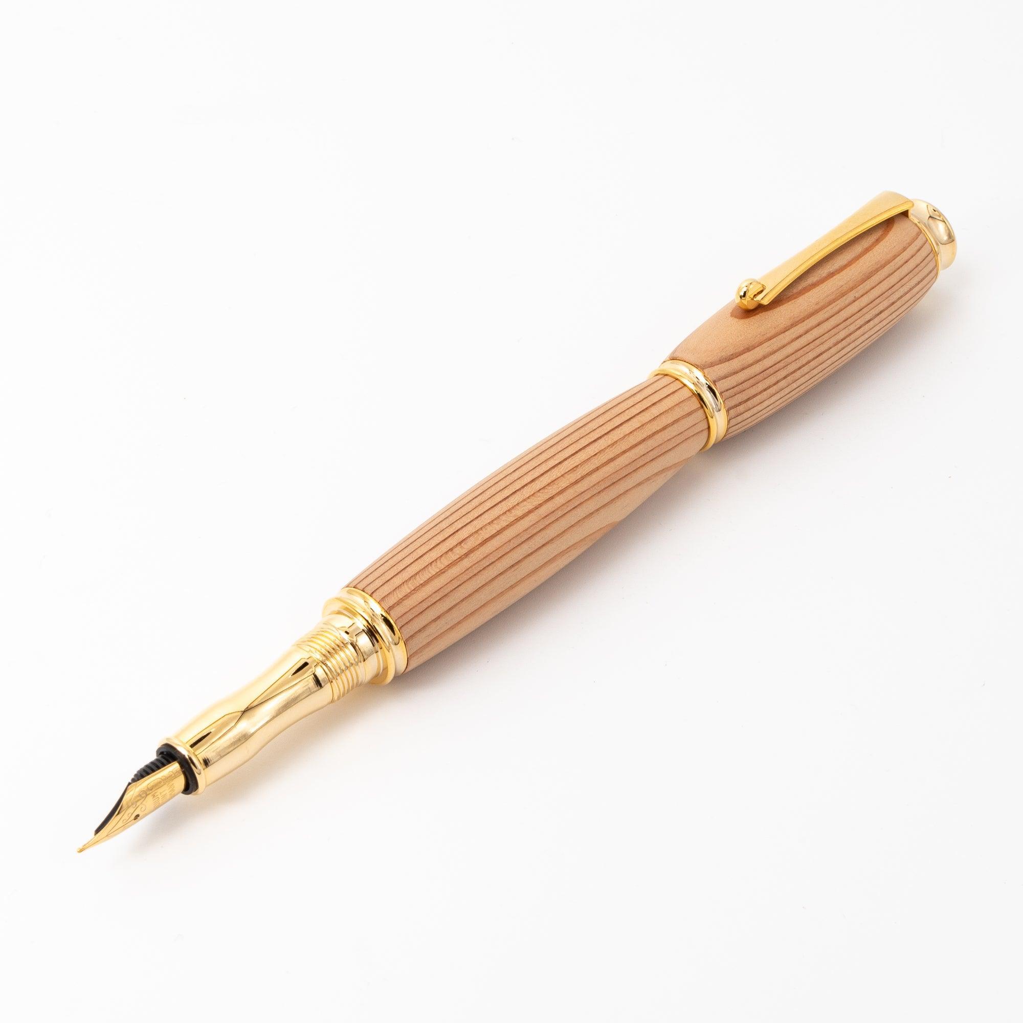 A Japanese fountain pen made of Yakushima cedar wood with gold accents, displayed open to highlight its nib and striped wood grain on a white surface.