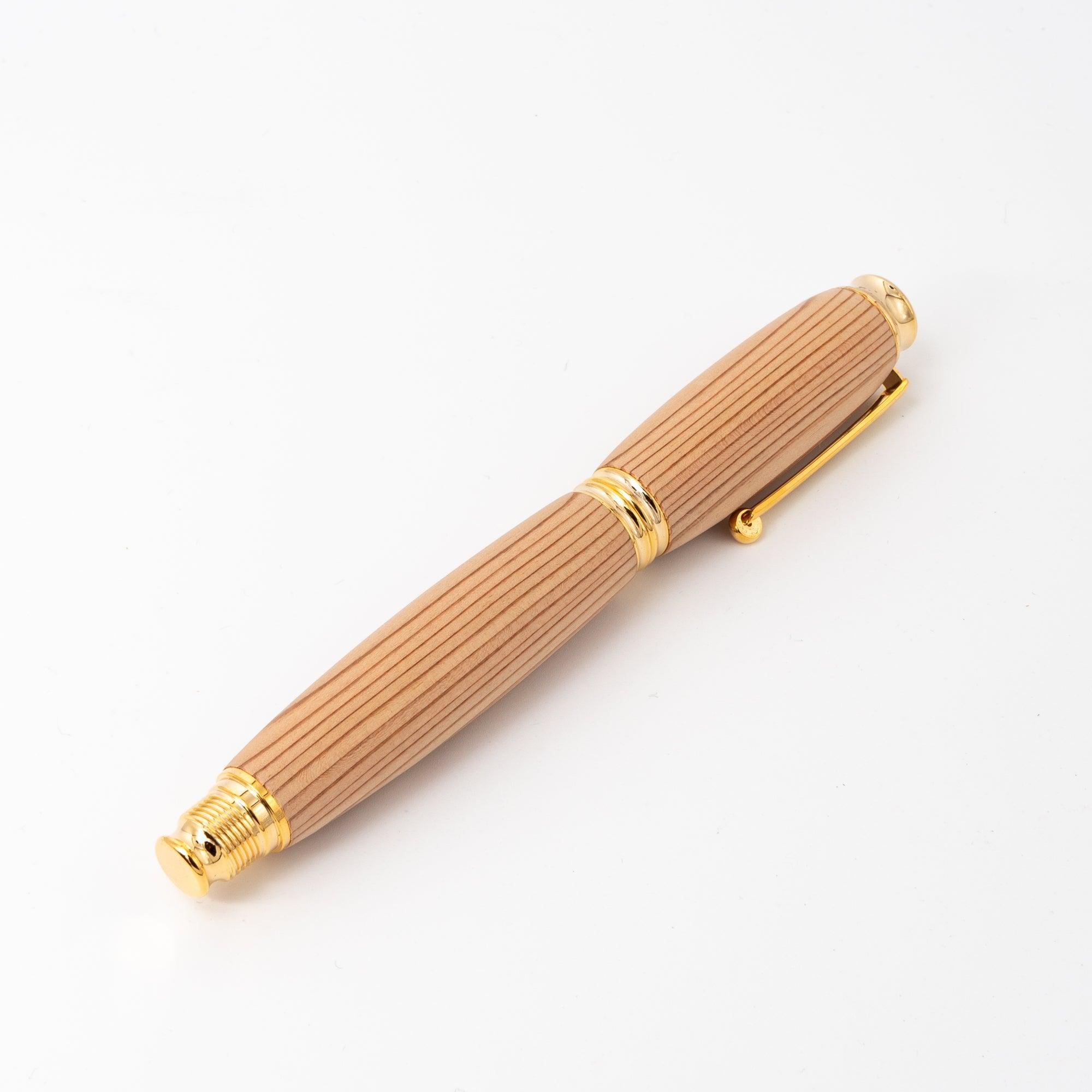 A Japanese fountain pen made of Yakushima cedar wood with gold accents, displayed horizontally on a white background, emphasizing its striped grain and elegance.