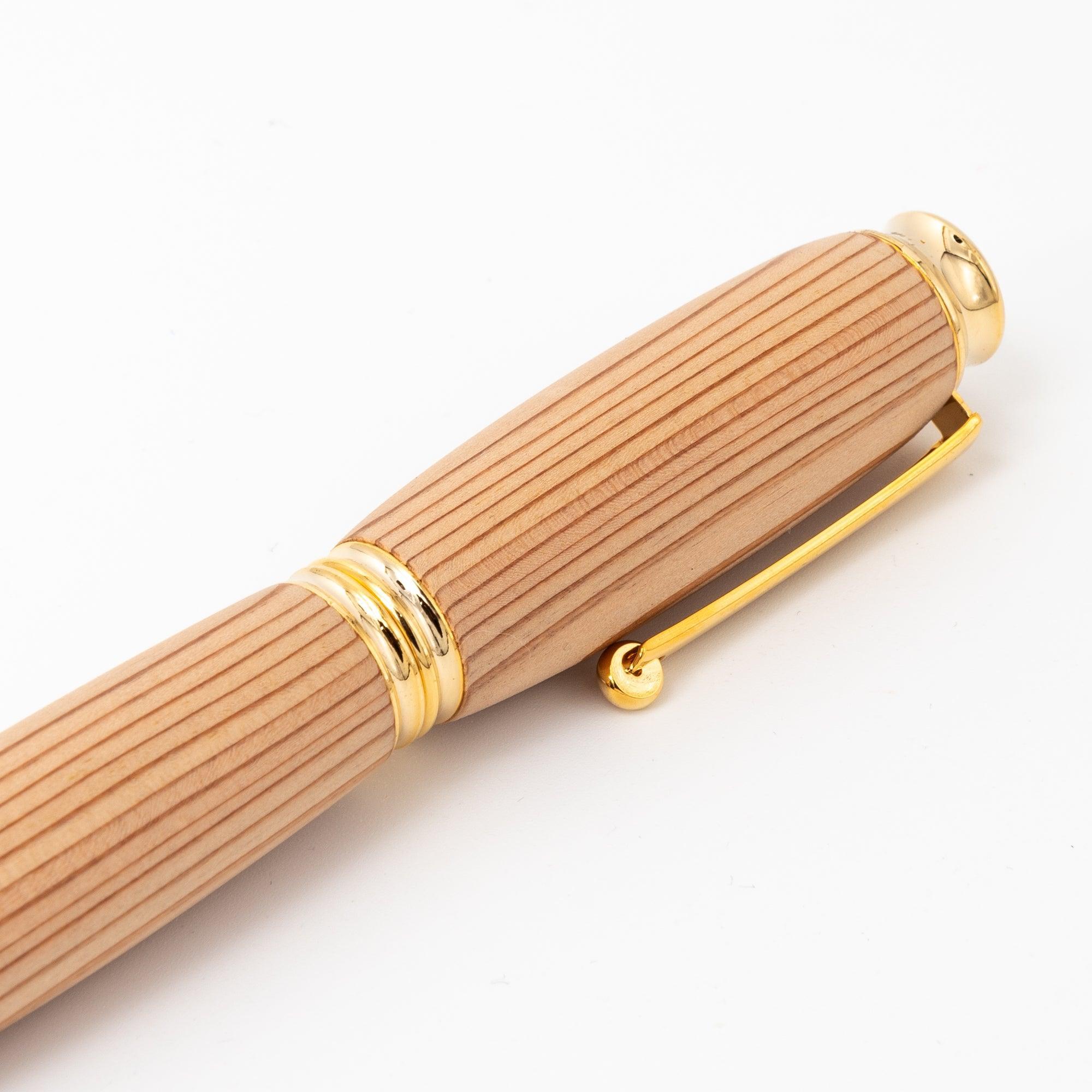 A close-up of a Japanese Yakushima cedar wood fountain pen showing its detailed gold clip and smooth, striped barrel on a clean white surface.