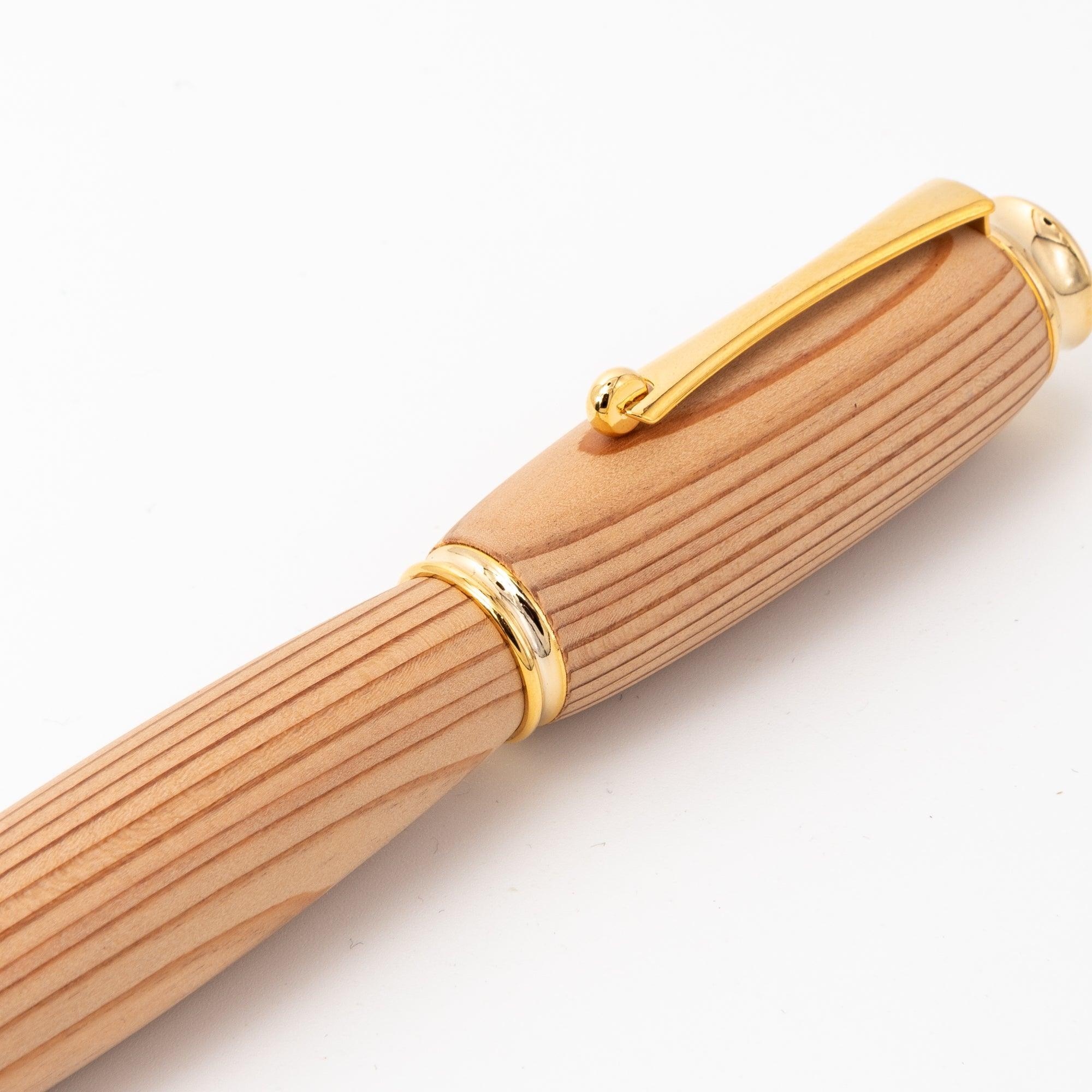 A detailed view of a Japanese fountain pen featuring a Yakushima cedar wood barrel and gold trim, highlighting its premium craftsmanship against a plain background.