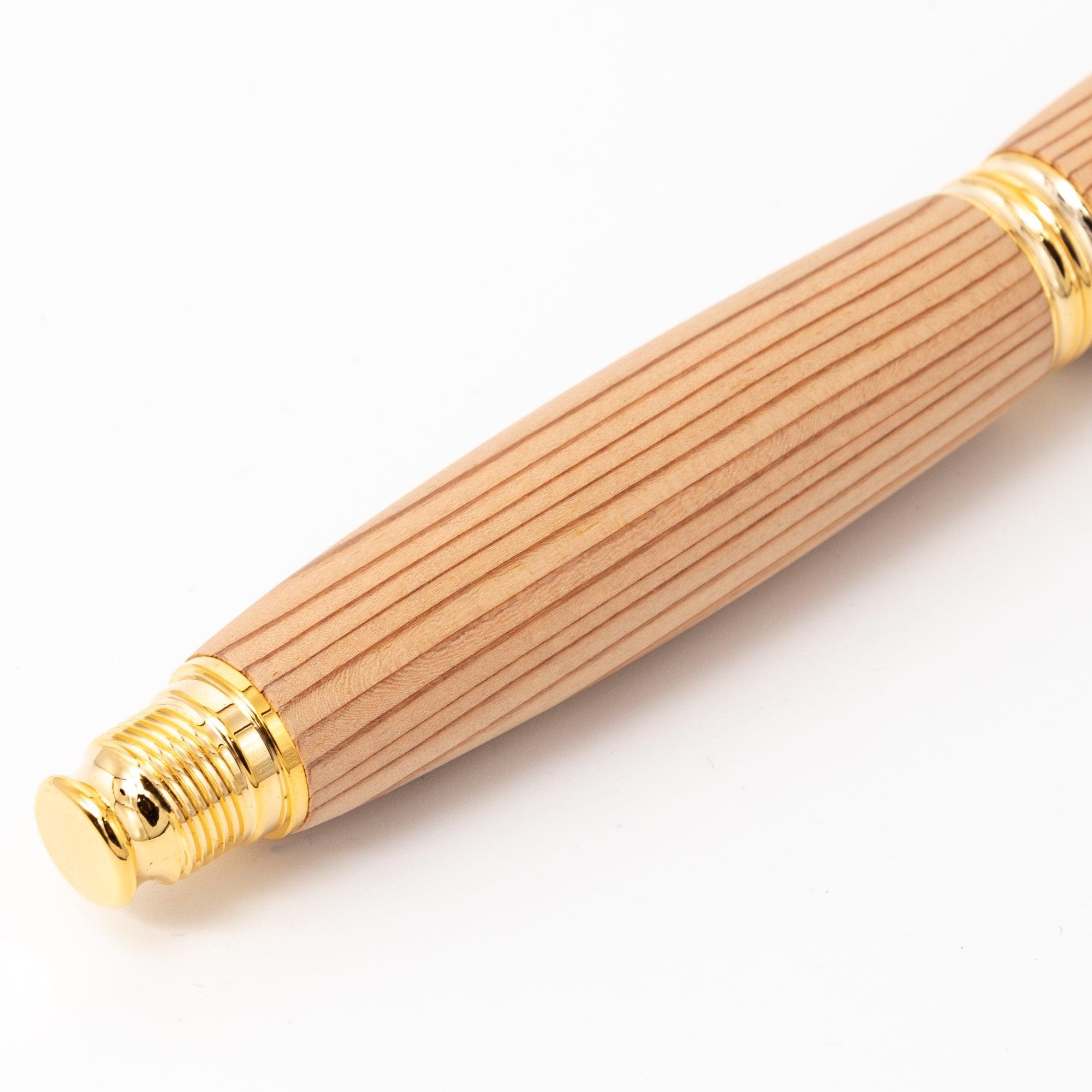 A detailed view of a Japanese fountain pen with a Yakushima cedar wood barrel and gold screw cap, highlighting its smooth striped texture on a white surface.