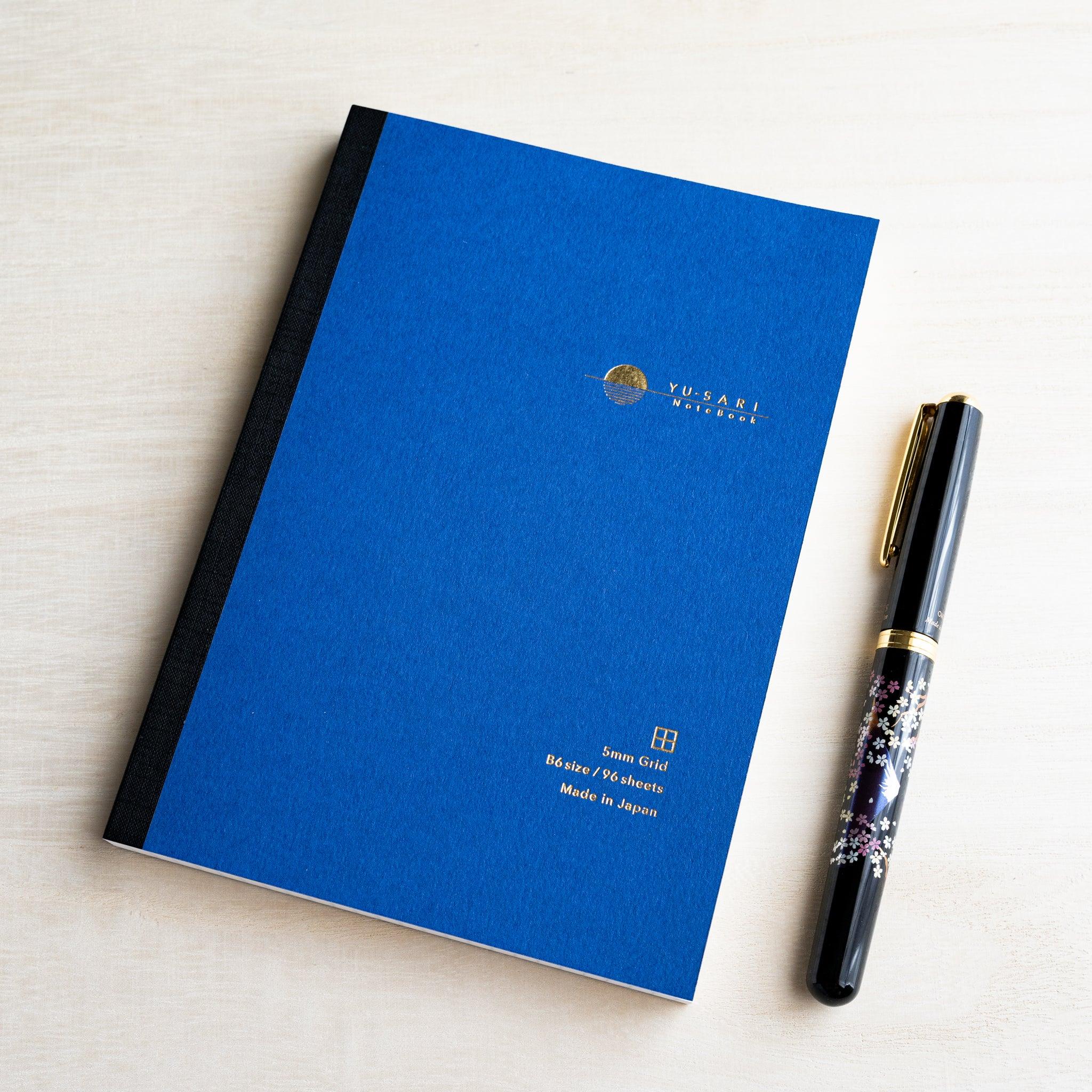 Blue B6 YU-SARI grid notebook on wood beside a black lacquer maki-e fountain pen, gold 5mm Grid, B6 size, 96 sheets text