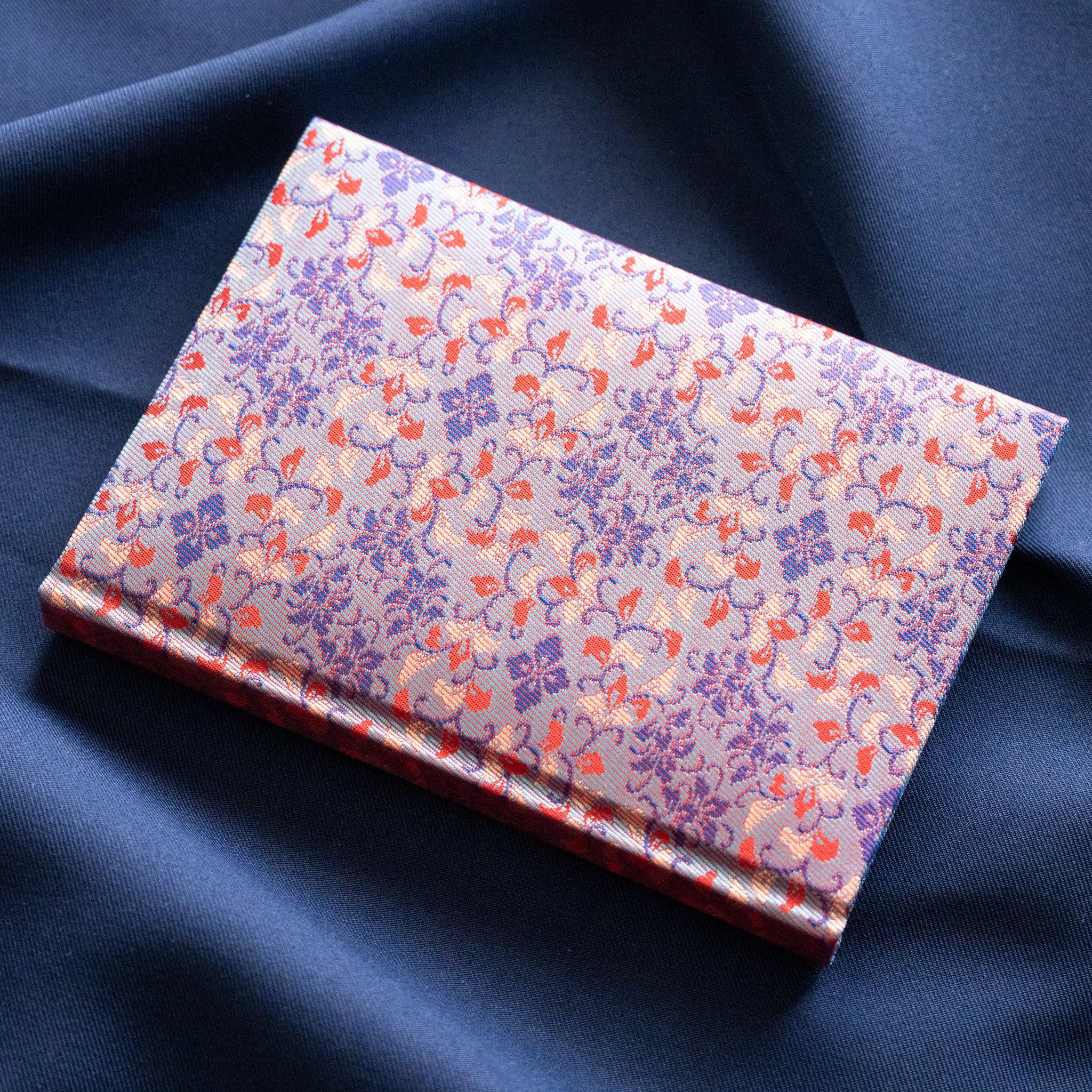 Yusoku Hanabishi Nishijin silk notebook lying flat, lavender-pink and red woven floral cover, no belly band, blue fabric