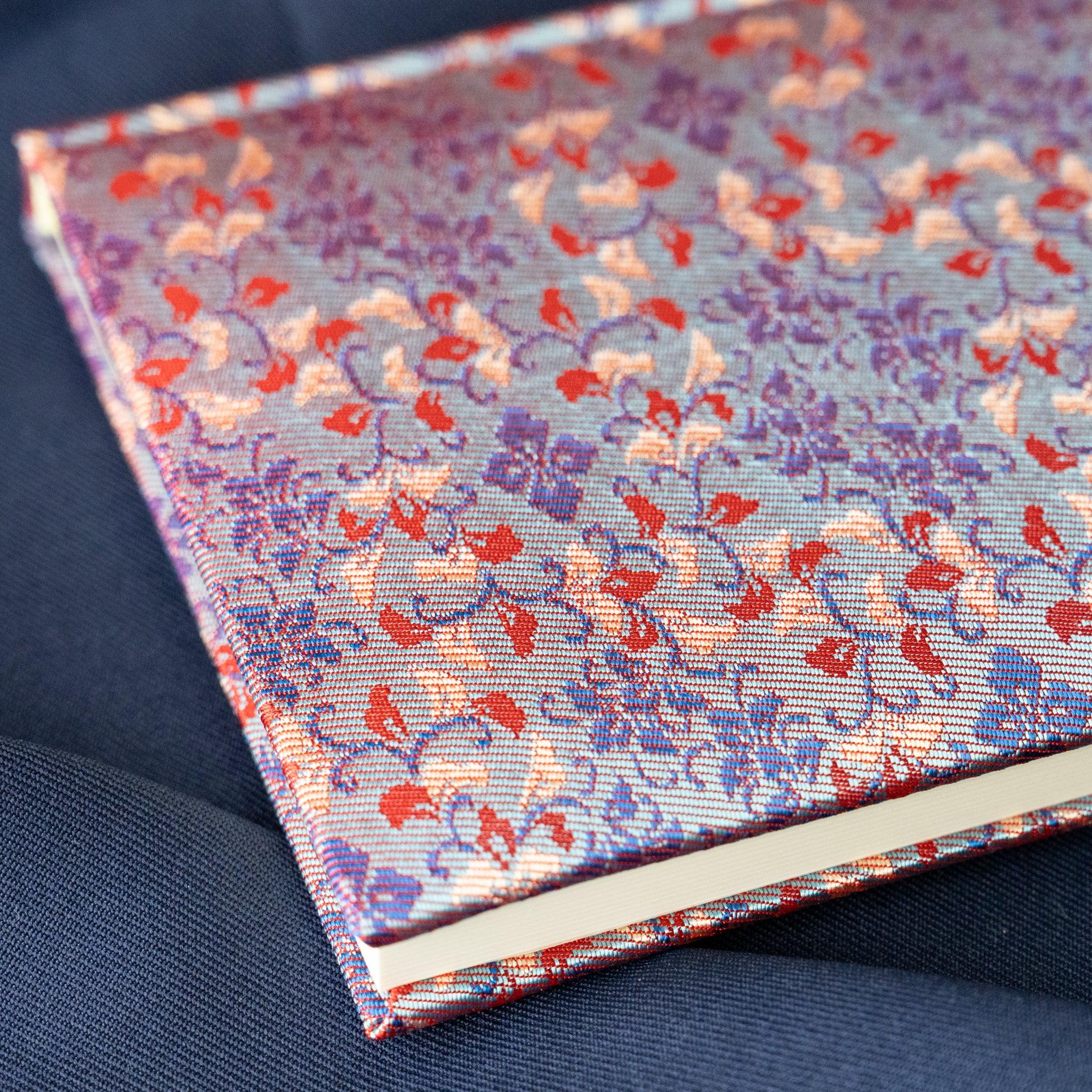 Yusoku Hanabishi Nishijin silk notebook cover corner close-up, lavender-pink and red floral pattern, white page edges