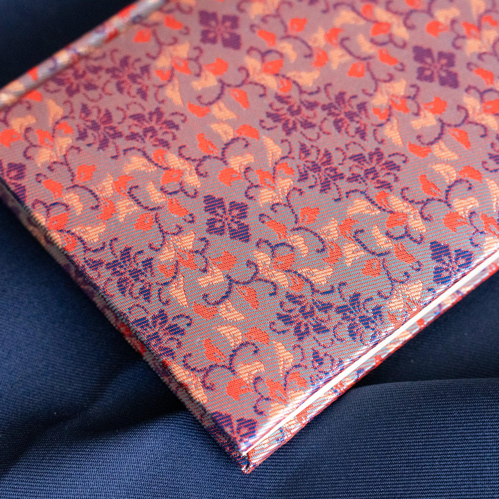 Yusoku Hanabishi Nishijin silk notebook cover close-up from above, lavender-pink and red floral pattern, page edges visible