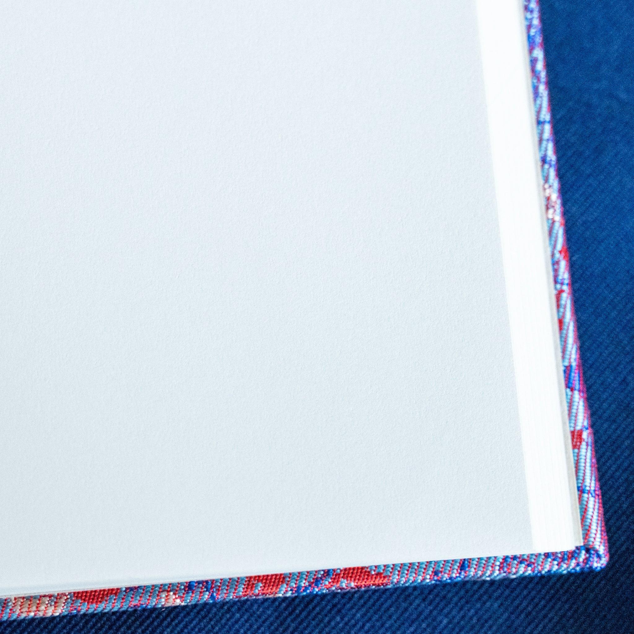 Yusoku Hanabishi Nishijin silk notebook corner detail showing lavender-pink woven cover edge against blue fabric background