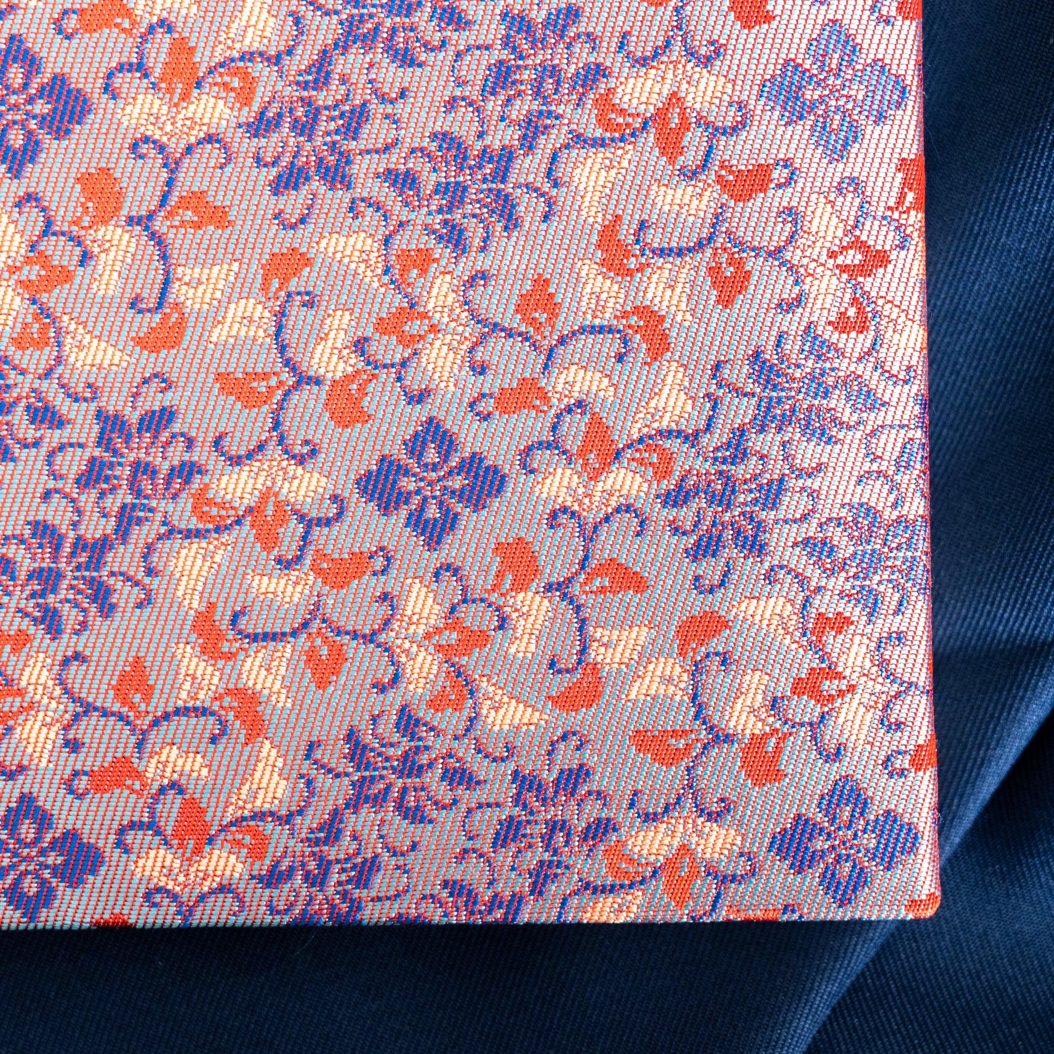 Close-up of Yusoku Hanabishi Nishijin silk cover, light ground with purple and red woven floral pattern, cover corner visible