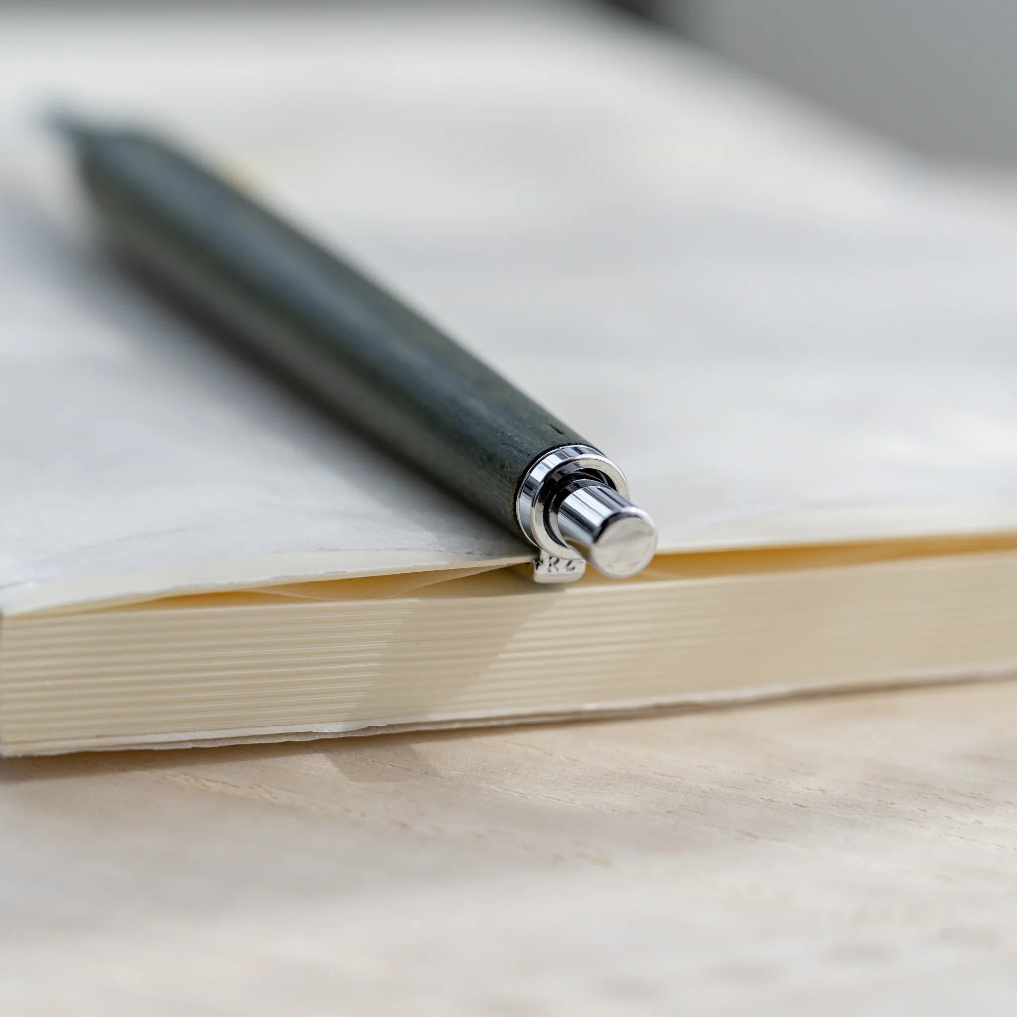 Zelkova wood urushi lacquered mechanical pencil in olive green resting on open notebook, Japanese keyaki wood