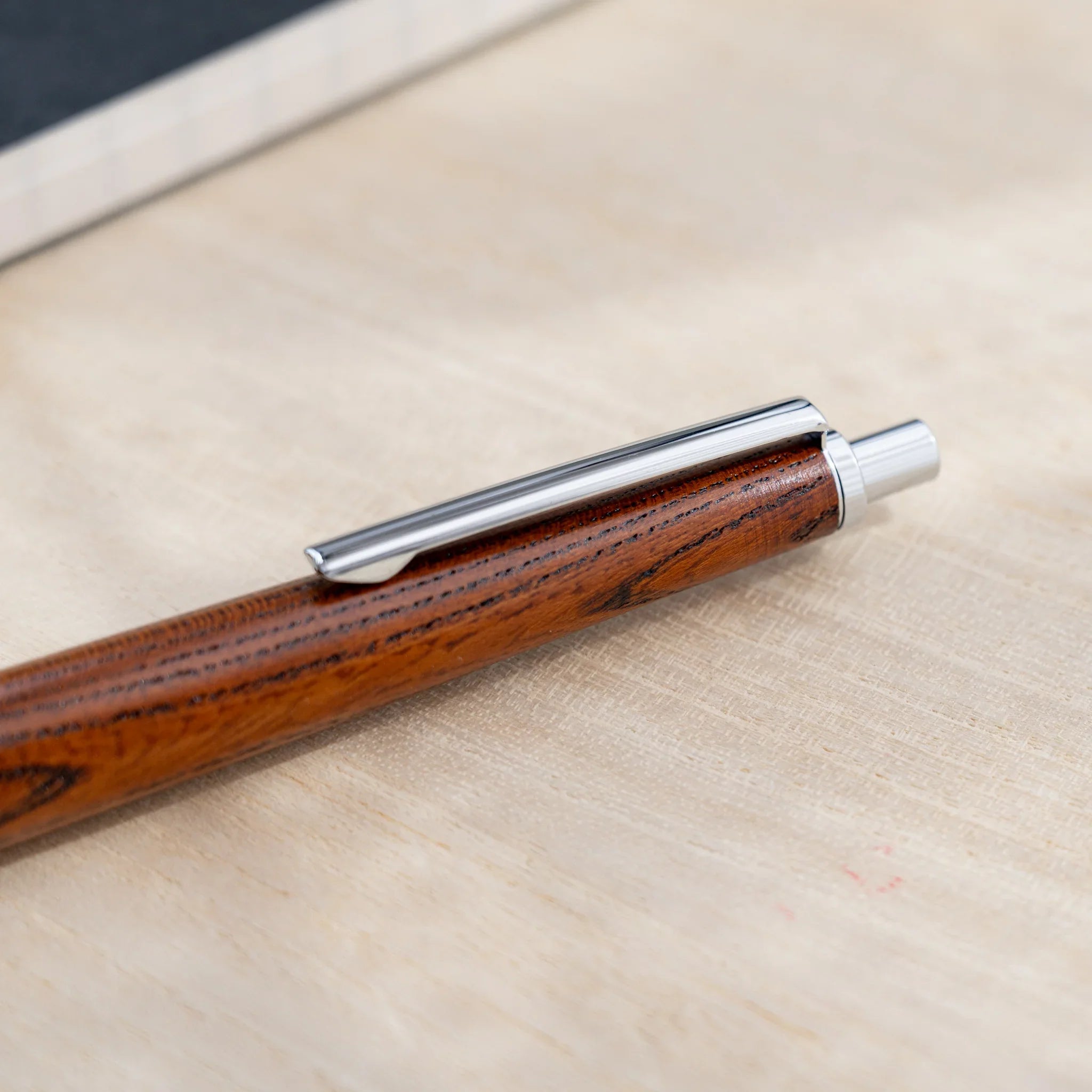 Amber-brown zelkova wood urushi mechanical pencil, close-up of knock end and silver clip, Japanese keyaki wood