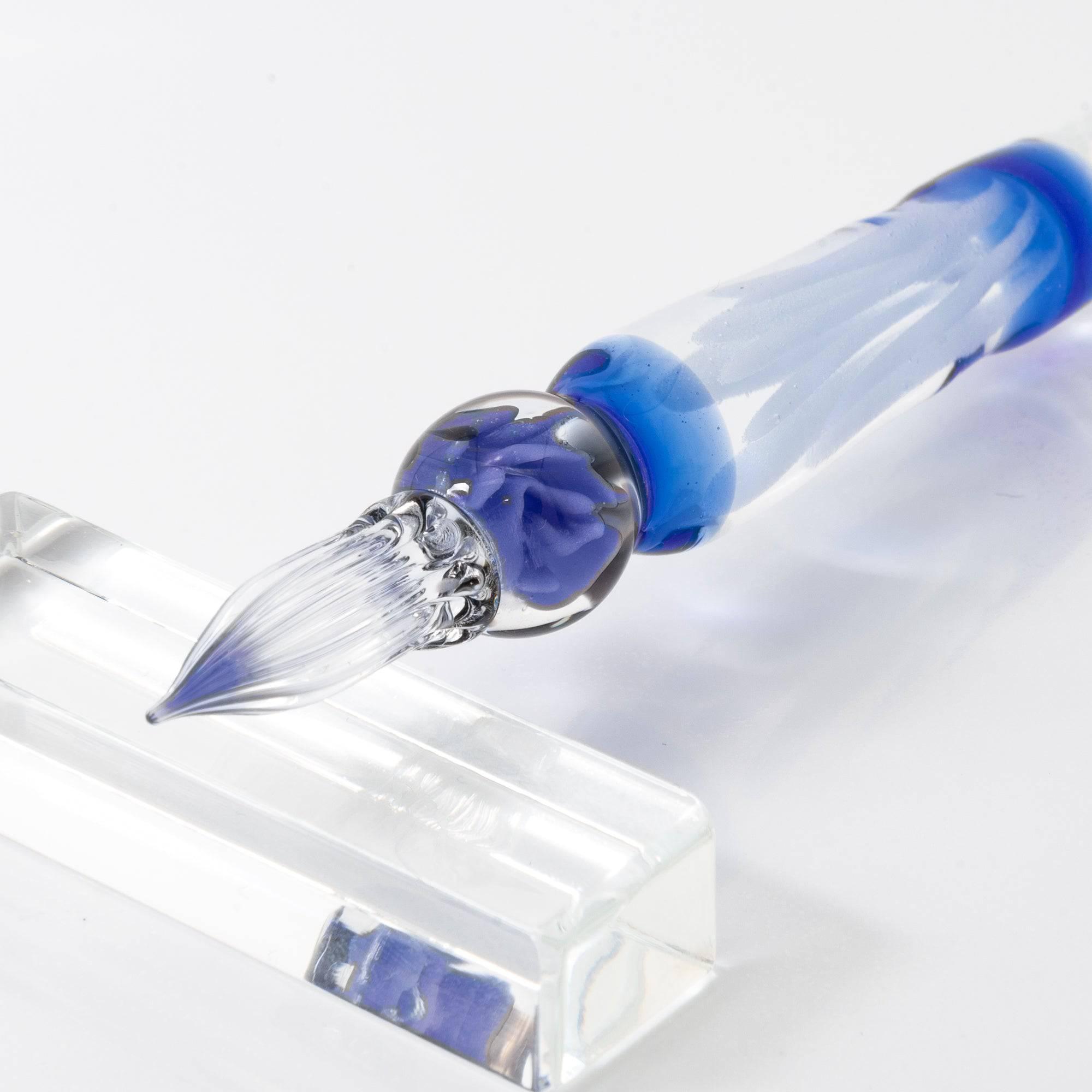 A delicate glass pen with an intricate blue rose motif, resting on a clear pen holder.