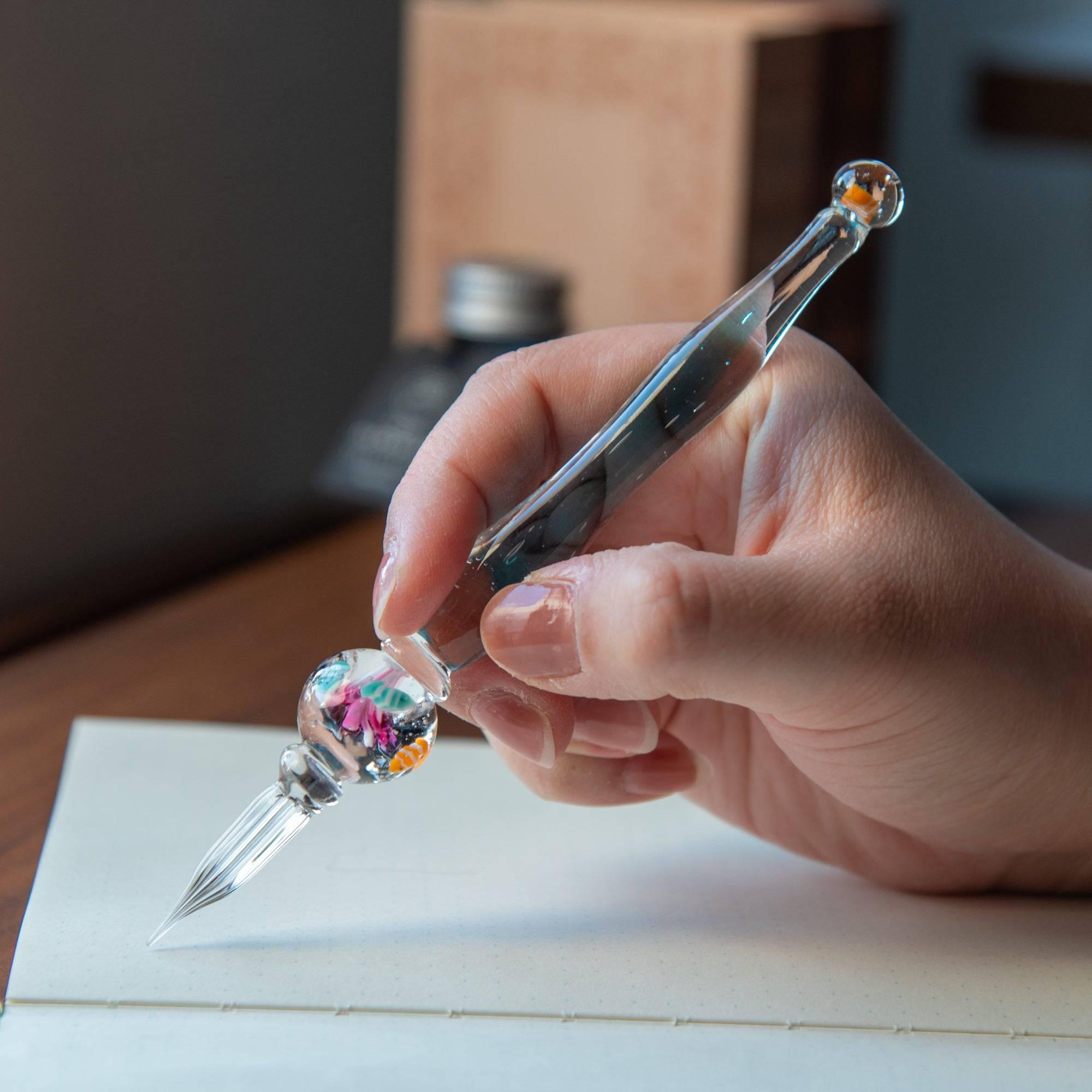 Hand holding a glass pen with clownfish motif inside a spherical aquarium-like design. Ideal for fans of Japanese stationery.