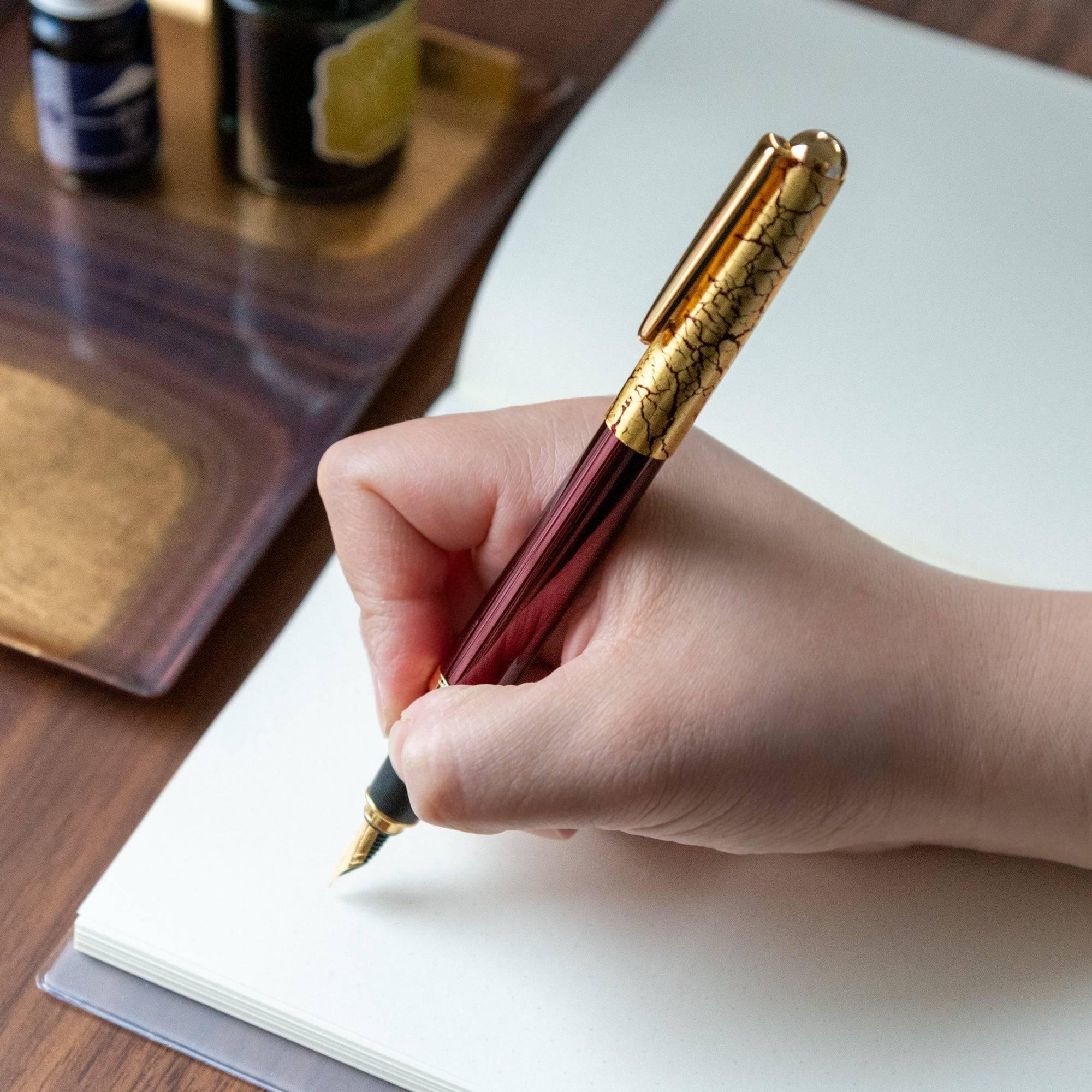 Handwriting with the wine-red fountain pen, showcasing the ergonomic grip and intricate crackled gold-leaf cap details.