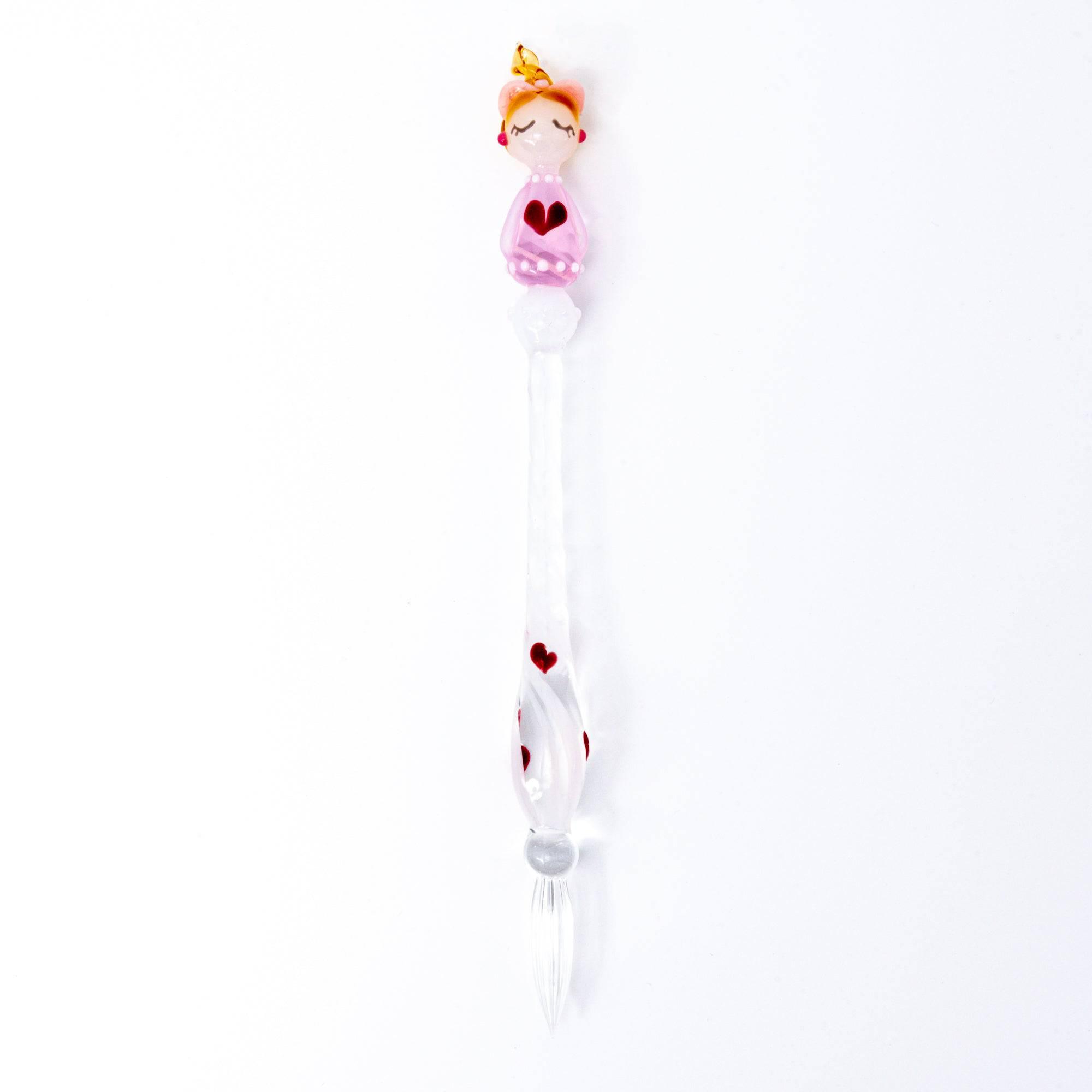 A top view of a Lovery-chan glass pen with a heart design, featuring a cute figure on top, dressed in pink with hearts along the pen shaft.