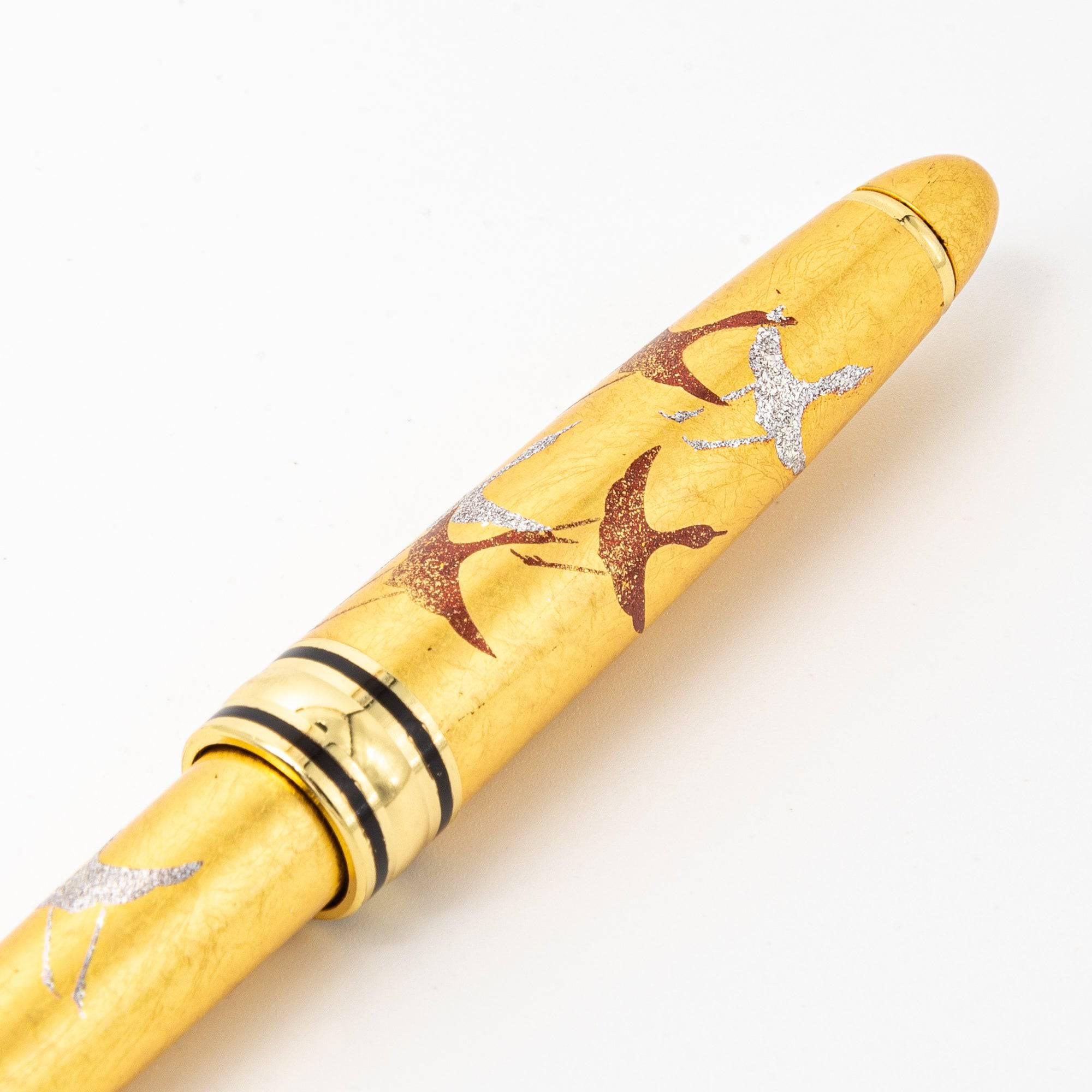 Close-up of the gold maki-e ballpoint pen showcasing intricate crane artwork in red and silver on the pen’s cap.