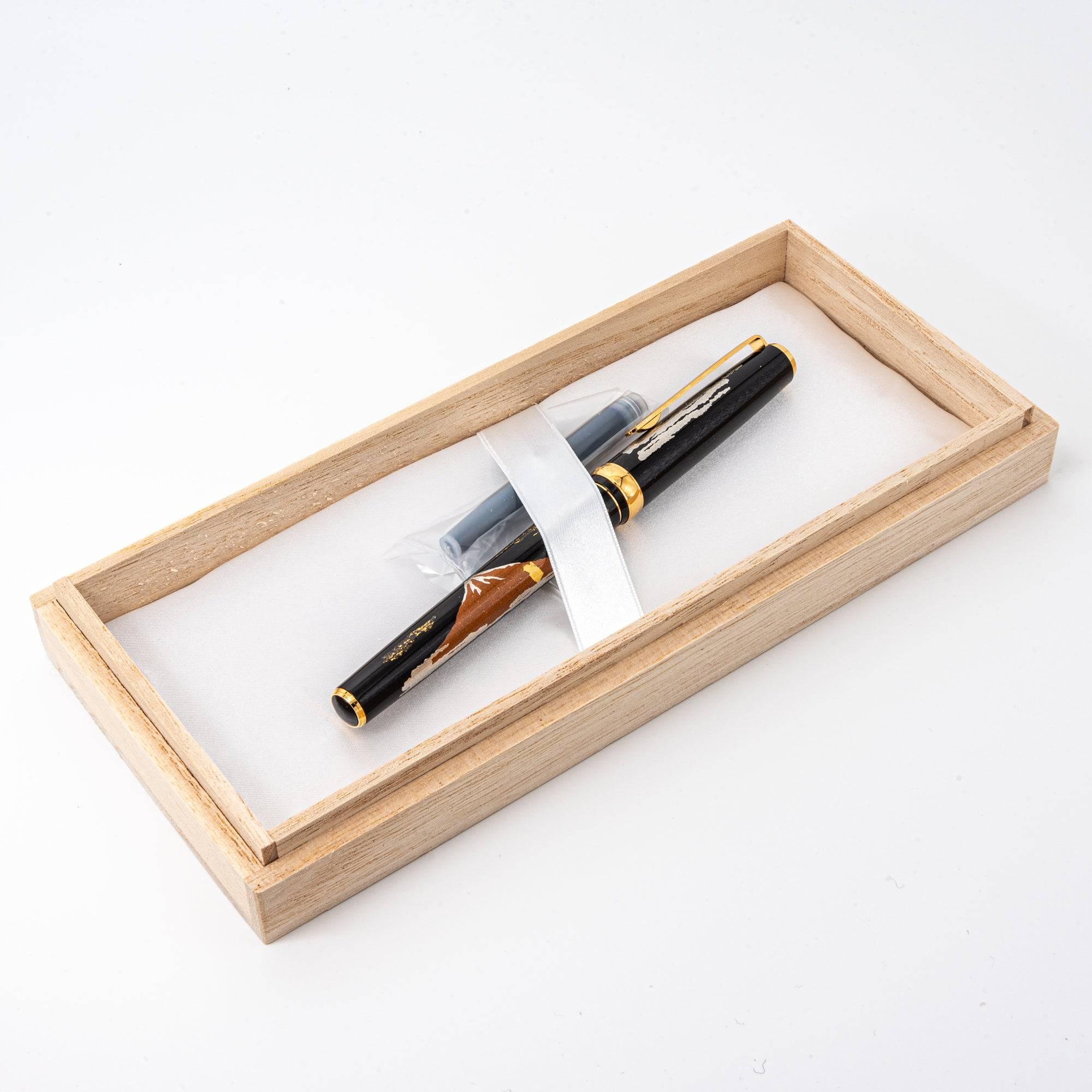 Japanese fountain pen with Mt. Fuji maki-e design, featuring gold and silver accents, in a wooden box with cartridges and protective fabric.