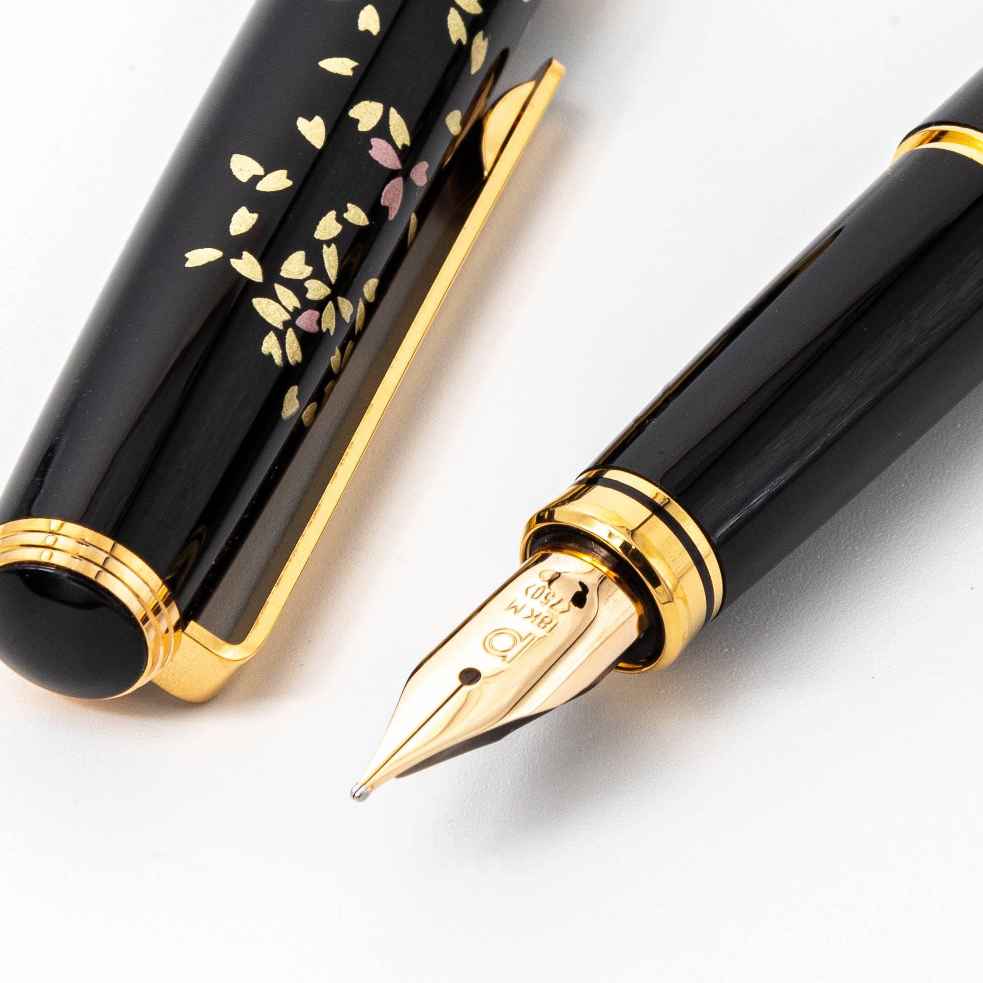 Japanese fountain pen with sakura design, gold and pink floral patterns on black lacquer, gold nib, photographed with hand on paper. (124文字)  