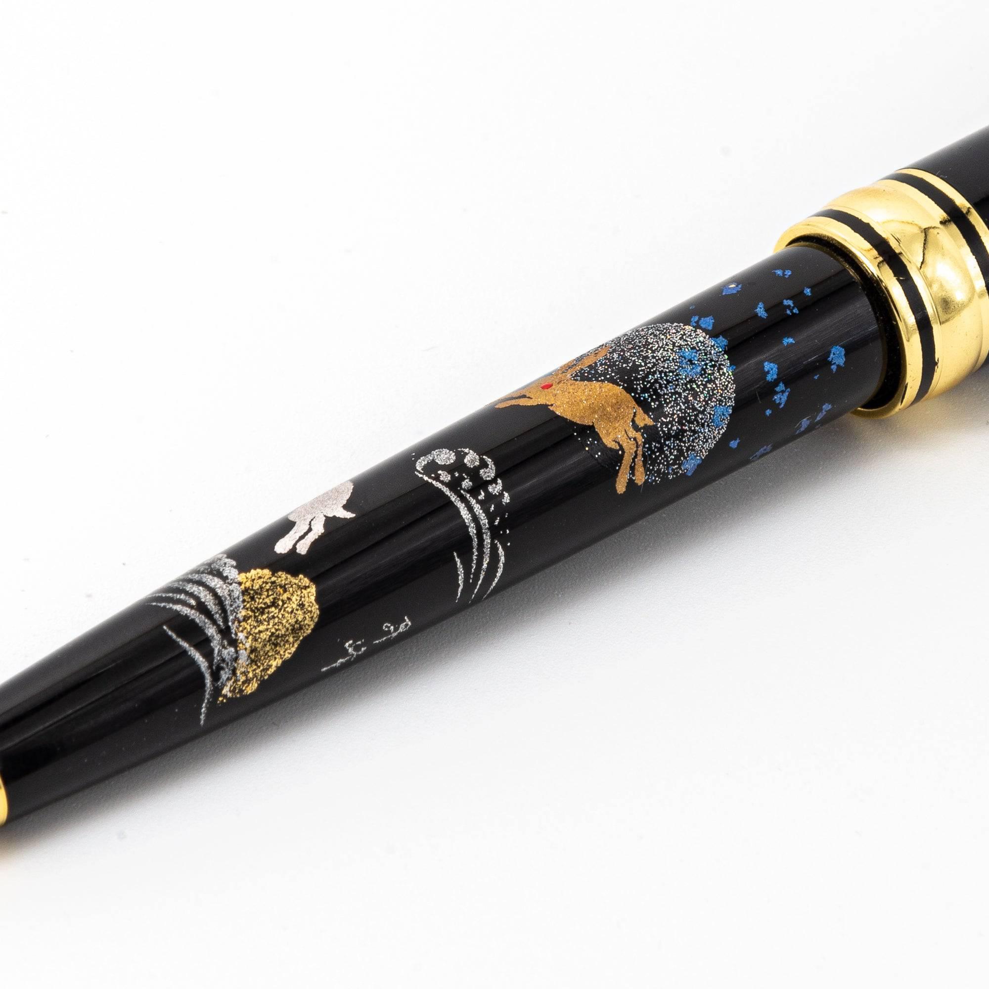 A close-up of a pen barrel showcasing detailed maki-e art of golden rabbits, silver waves, and a glittering moon on a glossy black surface.