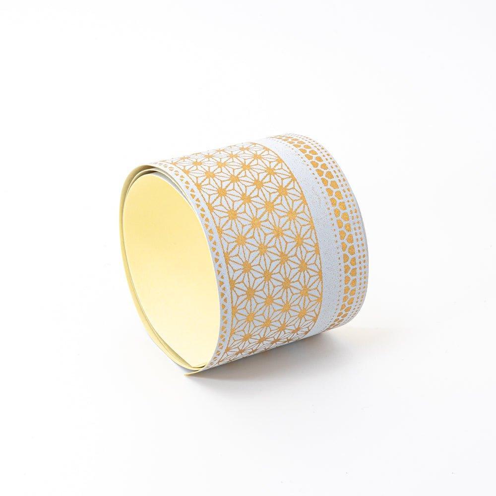 Rolled Japanese stationery washi tape with gold geometric patterns and white accents on a light background, displayed on a plain surface.  