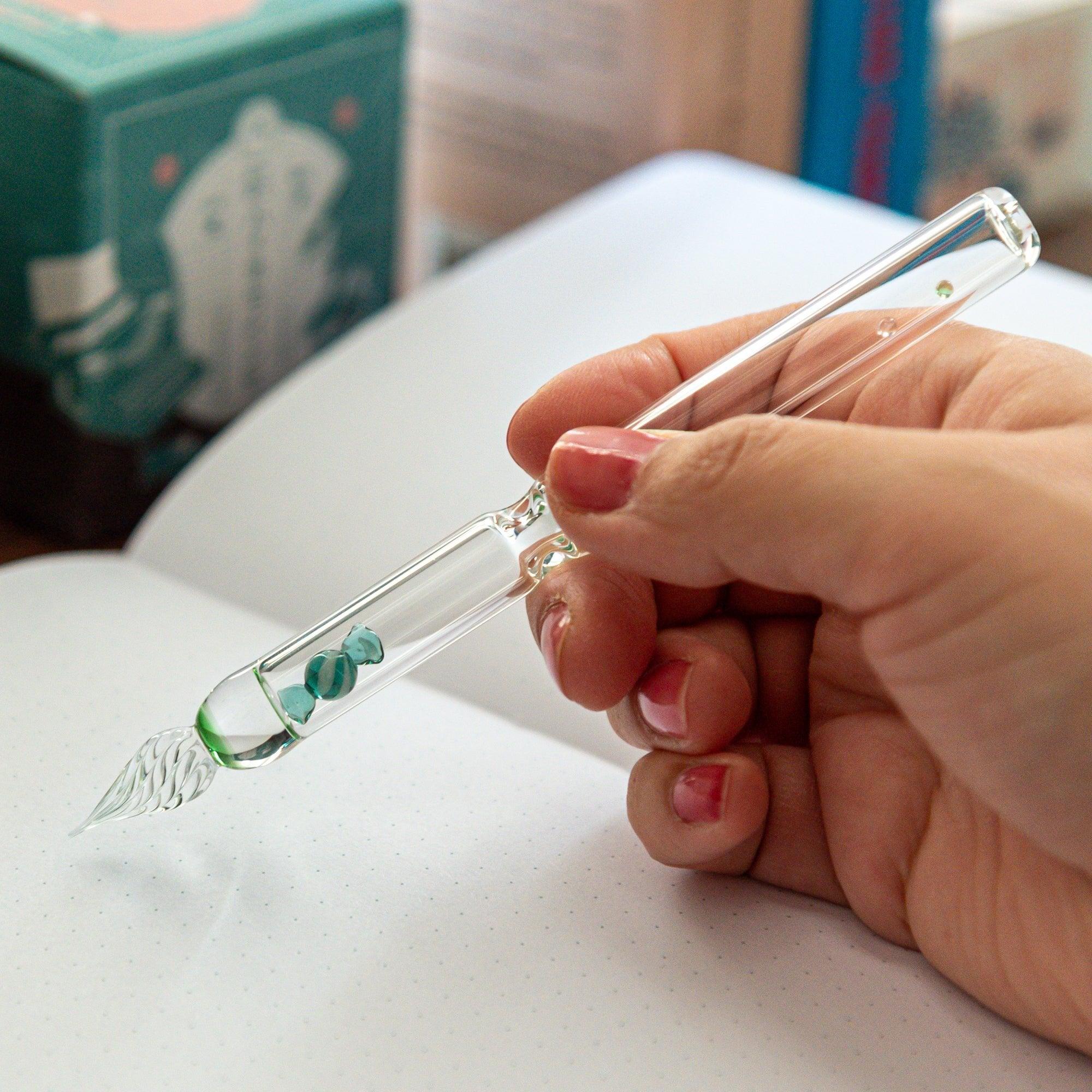 This glass pen with a green candy inside is held in hand, showcasing its sleek design and playful candy motif for a smooth writing experience.