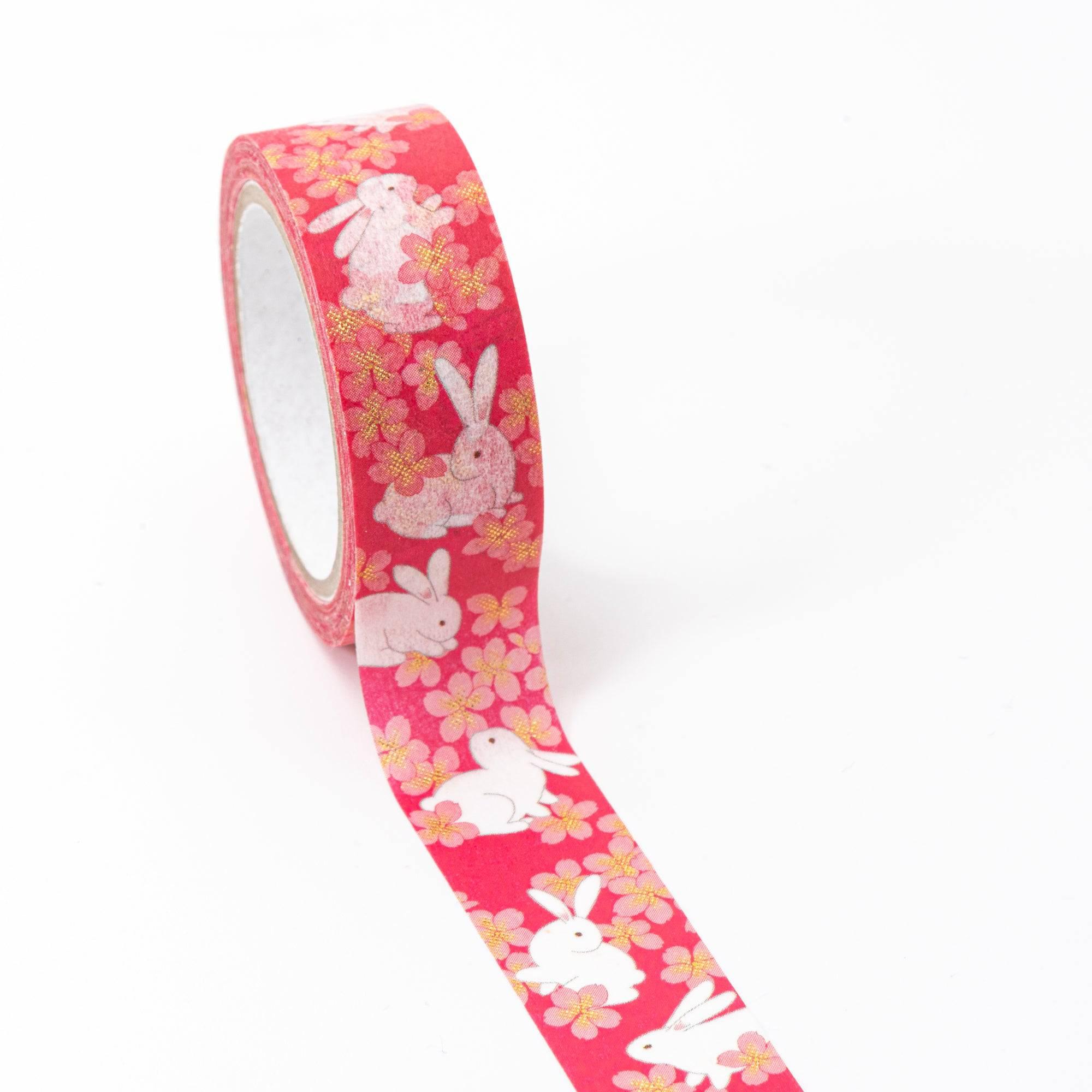 Roll of Iyo Washi Tape with sakura rabbits designs, unraveling to reveal its whimsical motifs, placed on a wooden surface under soft lighting.  