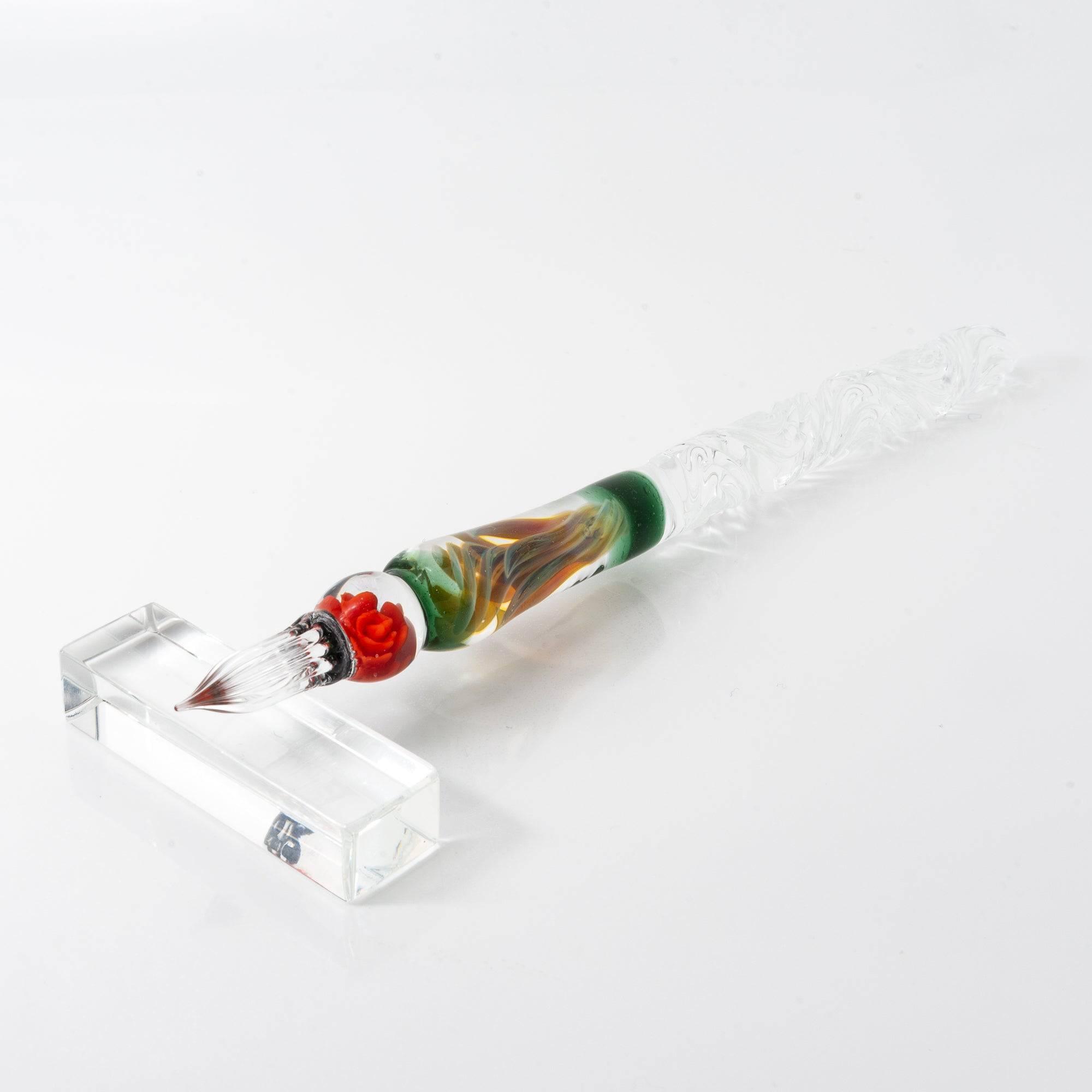 A delicate glass pen with an intricate orange rose motif, resting on a clear pen holder.