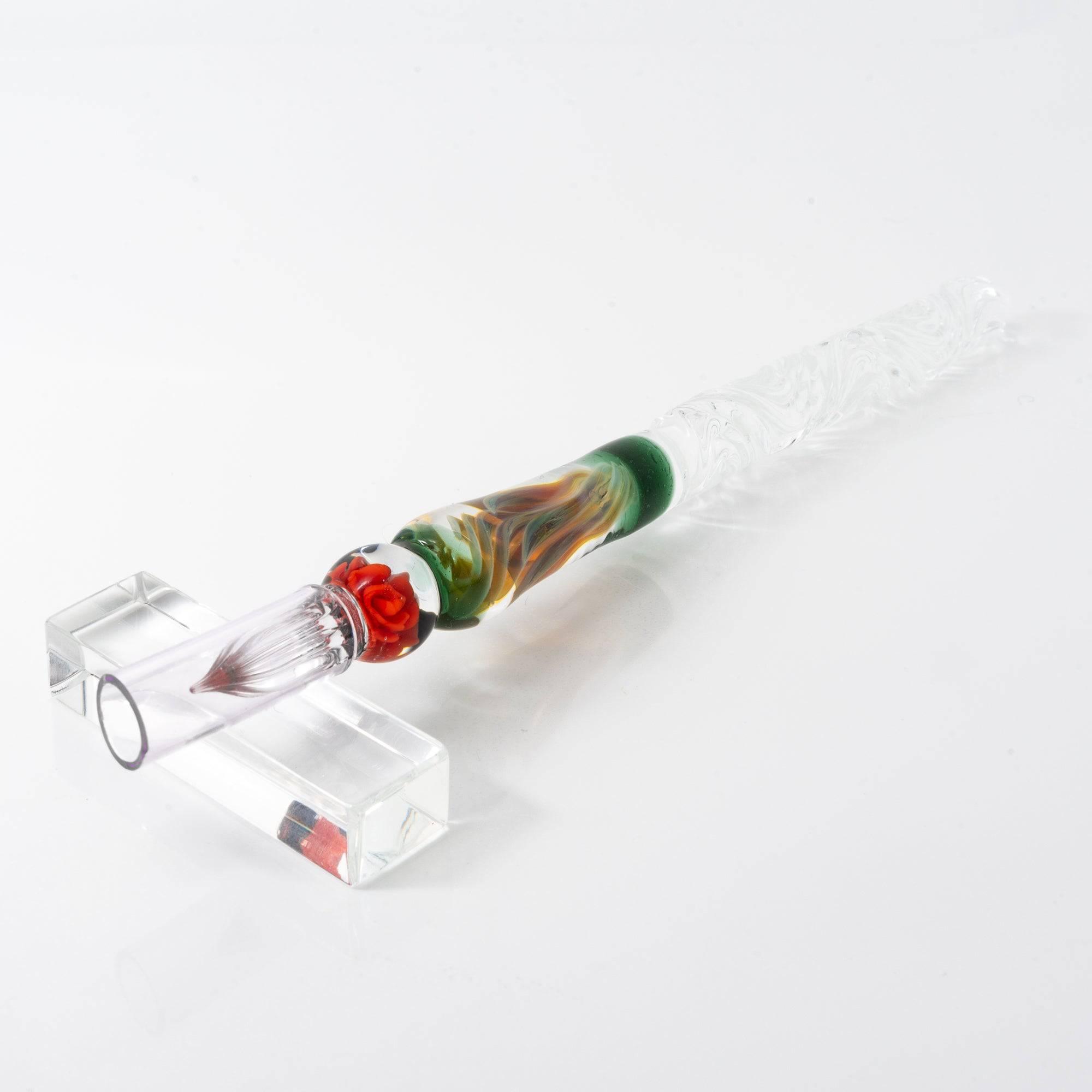 A delicate glass pen with an intricate orange rose motif, resting on a clear pen holder.