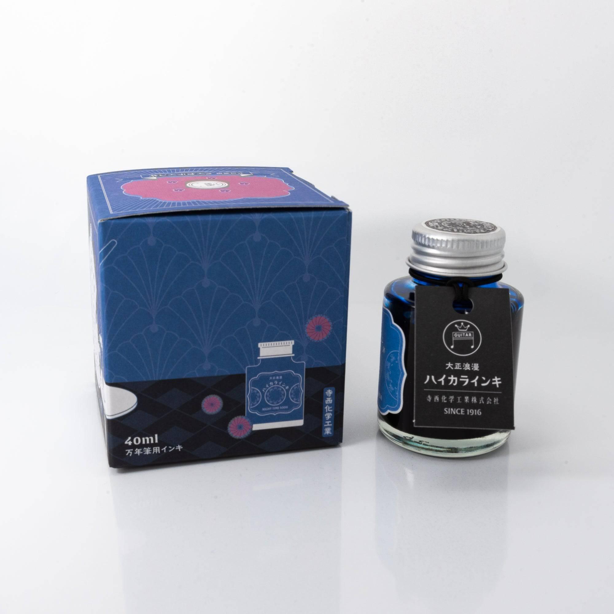 Open Taisho Romance Nighttime Soda ink bottle with luminous blue liquid, placed beside a fountain pen, blending style and practicality.  