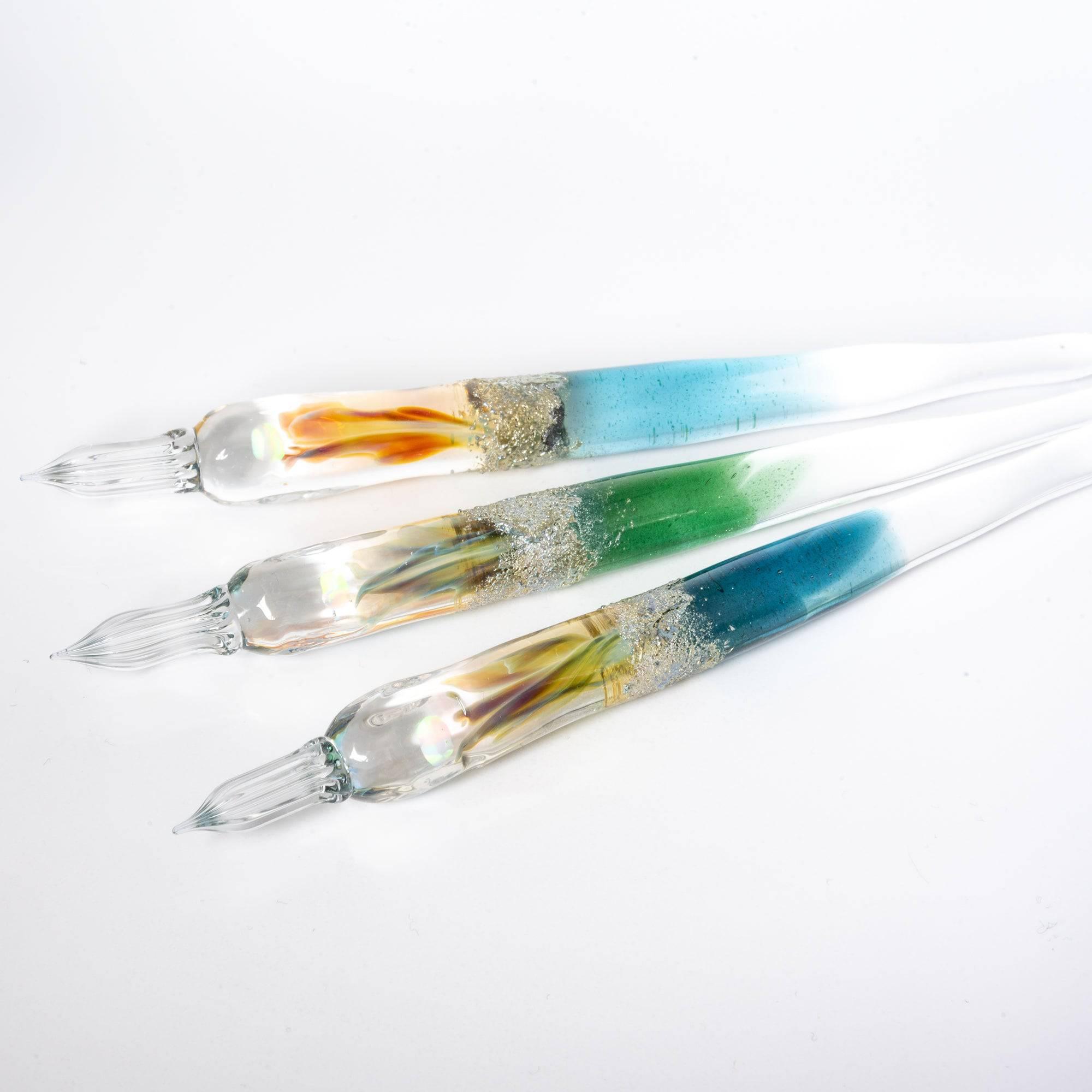 Three glass pens with light blue, green, and clear gradients, suspended opals, and silver accents, displayed in sunlight for a luxurious look.