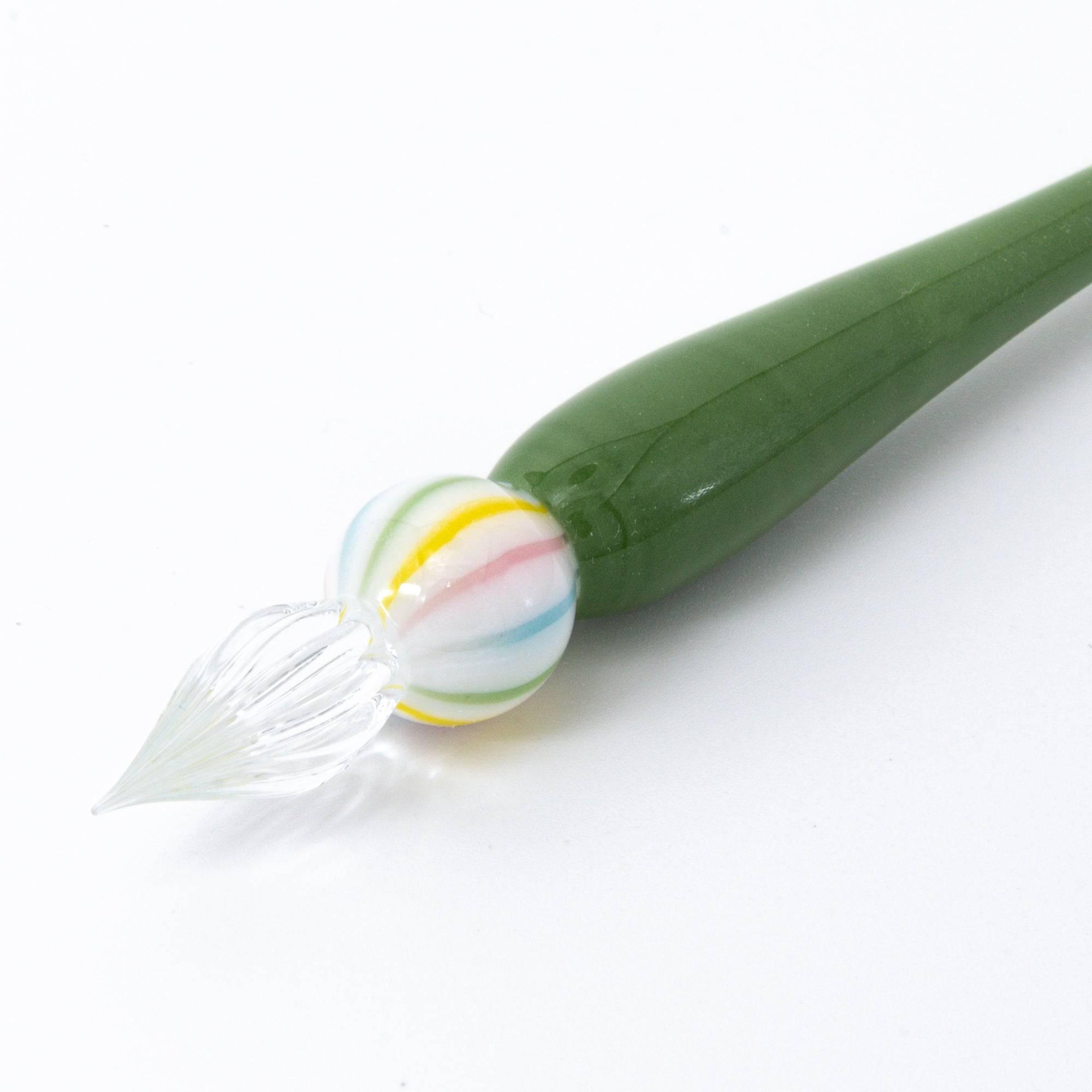 A close-up of a green matcha color glass pen with a colorful marble-like detail on both ends, resting on a clean, white background.