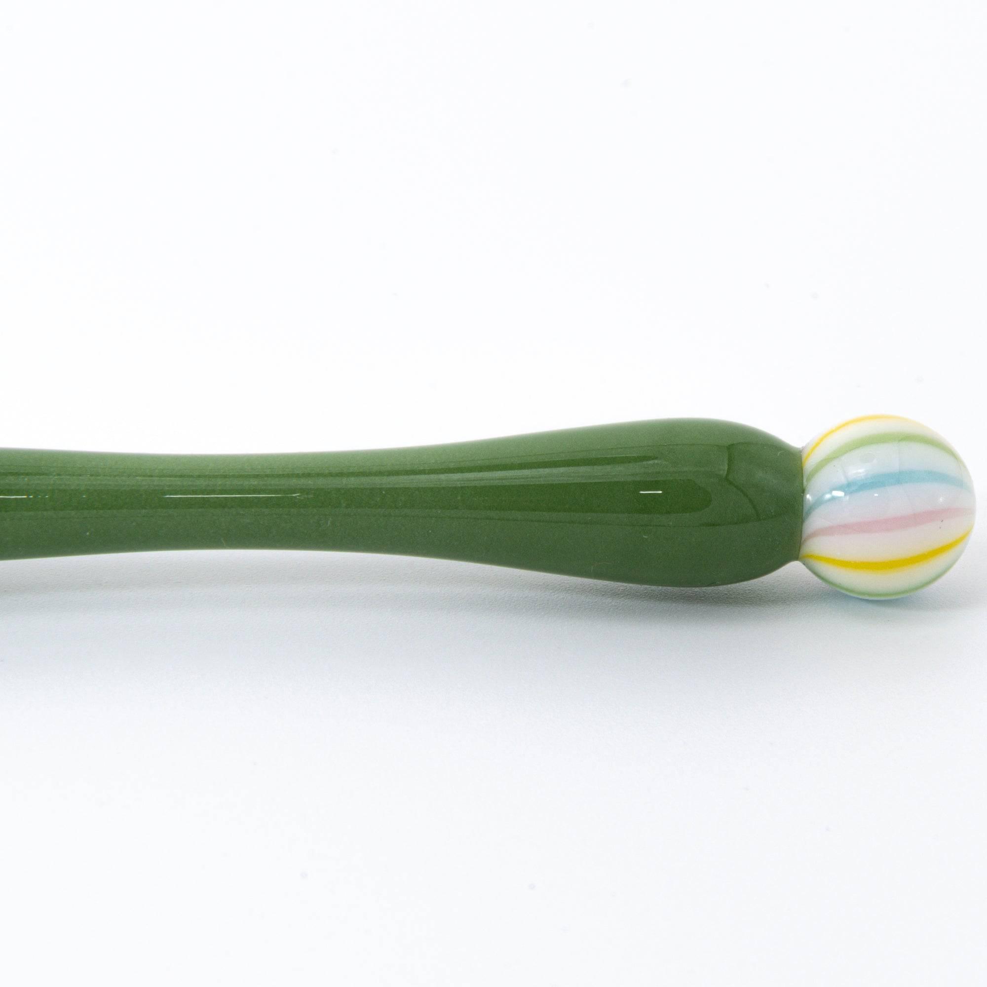 A close-up of a green matcha color glass pen with a colorful marble-like detail on both ends, resting on a clean, white background.