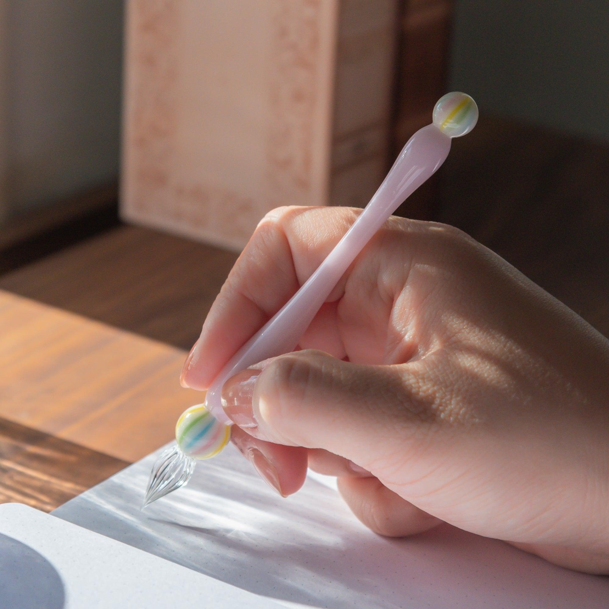 Hand holding a pink glass pen inspired by Japanese wagashi, featuring marble-like glass beads at each end, perfect for delicate and creative writing.